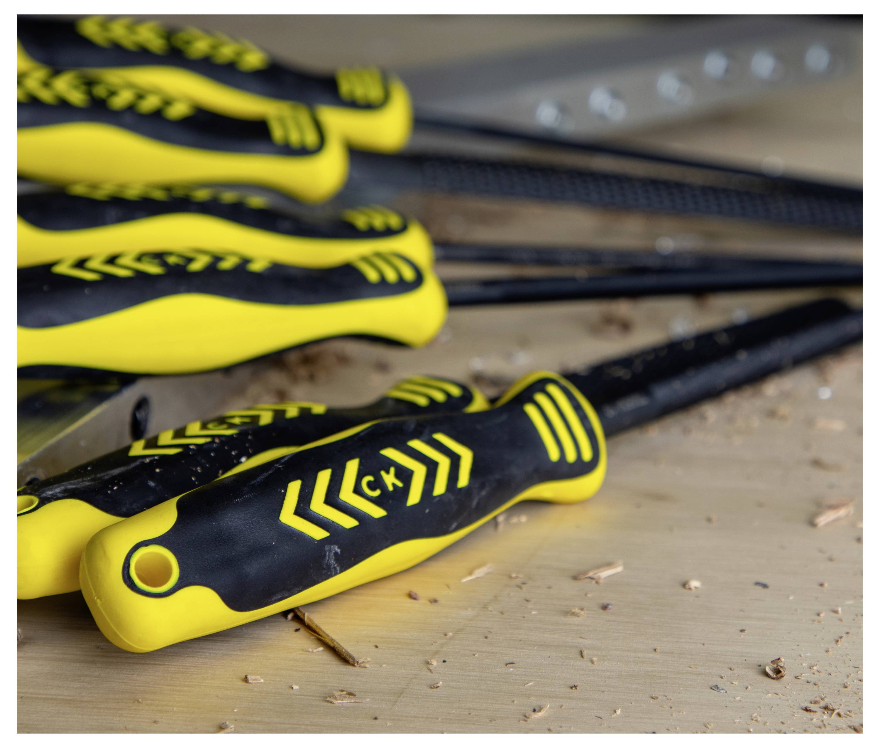 Un ensemble de limes aux manches noirs et jaunes repose sur une surface en bois avec des copeaux de bois, suggérant une activité de travail du bois.