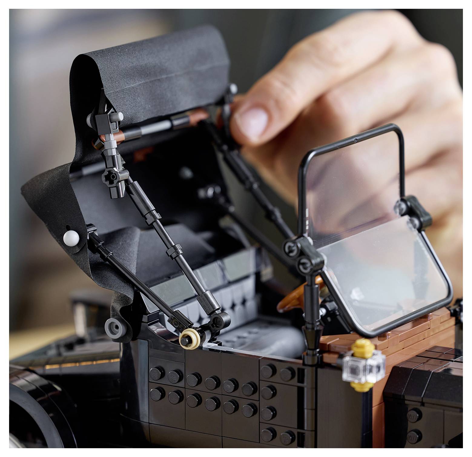 A close-up of a hand opening the canopy of a detailed LEGO model of a classic sports car, showcasing intricate assembly and design.
