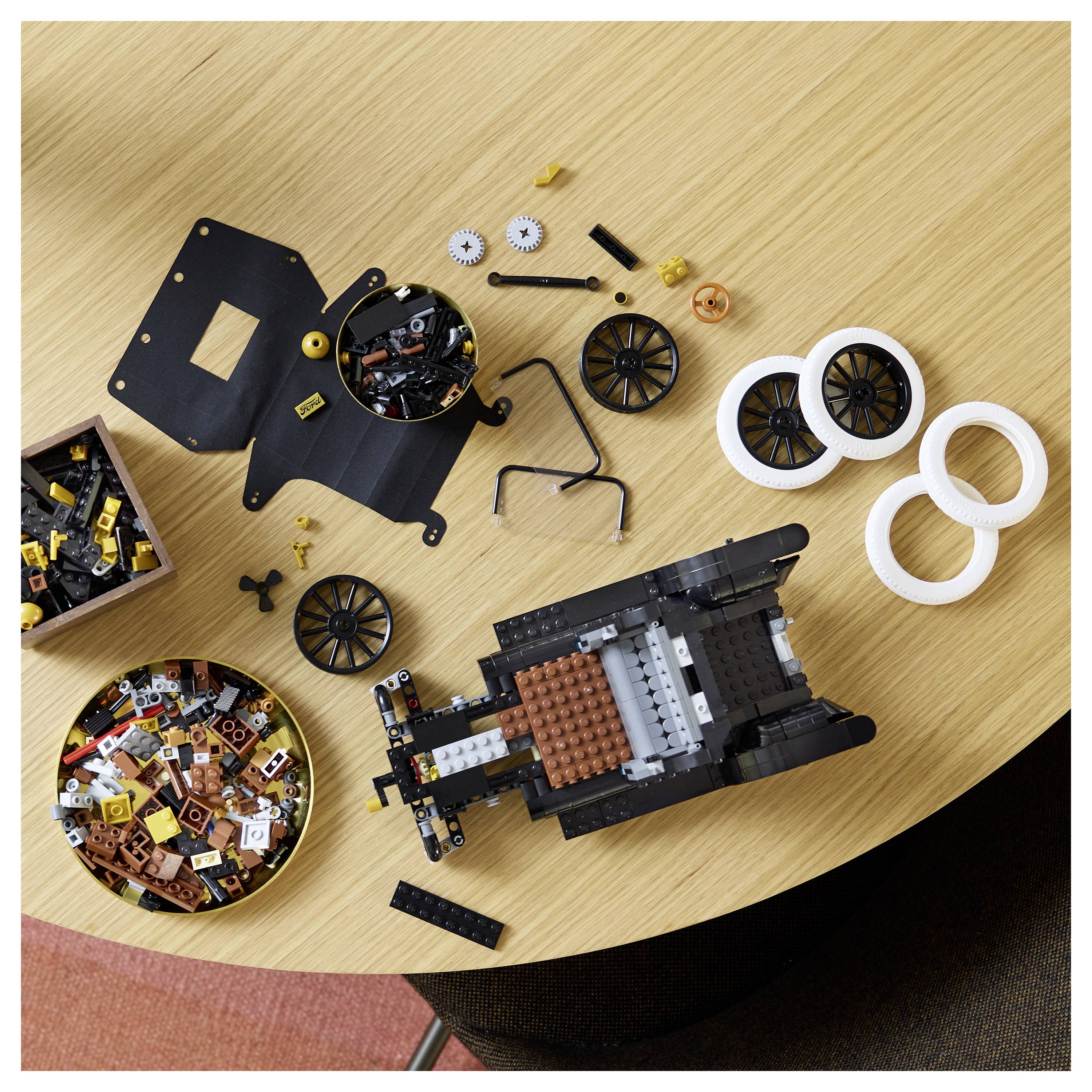 Lego pieces and partially assembled vehicle on a wooden table, including wheels, gears, and various small blocks.