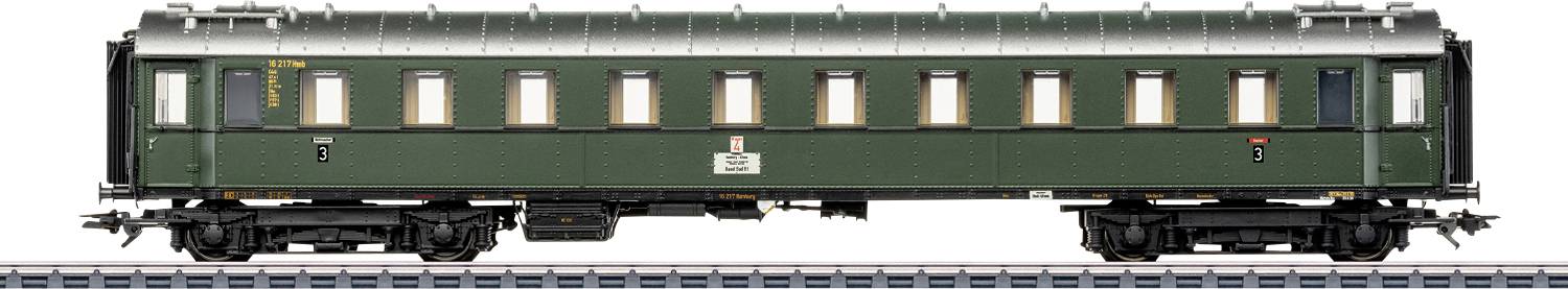 Un wagon de passagers de train vintage de couleur verte avec une rangée de fenêtres est stationné sur une voie, mettant en évidence des éléments de design classiques typiques des débuts des voyages ferroviaires.