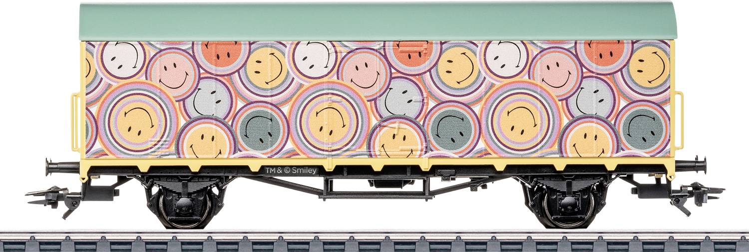 Un wagon de train avec des visages souriants colorés et des motifs circulaires. Le toit est vert, et le wagon est sur une voie ferrée, vu de côté.
