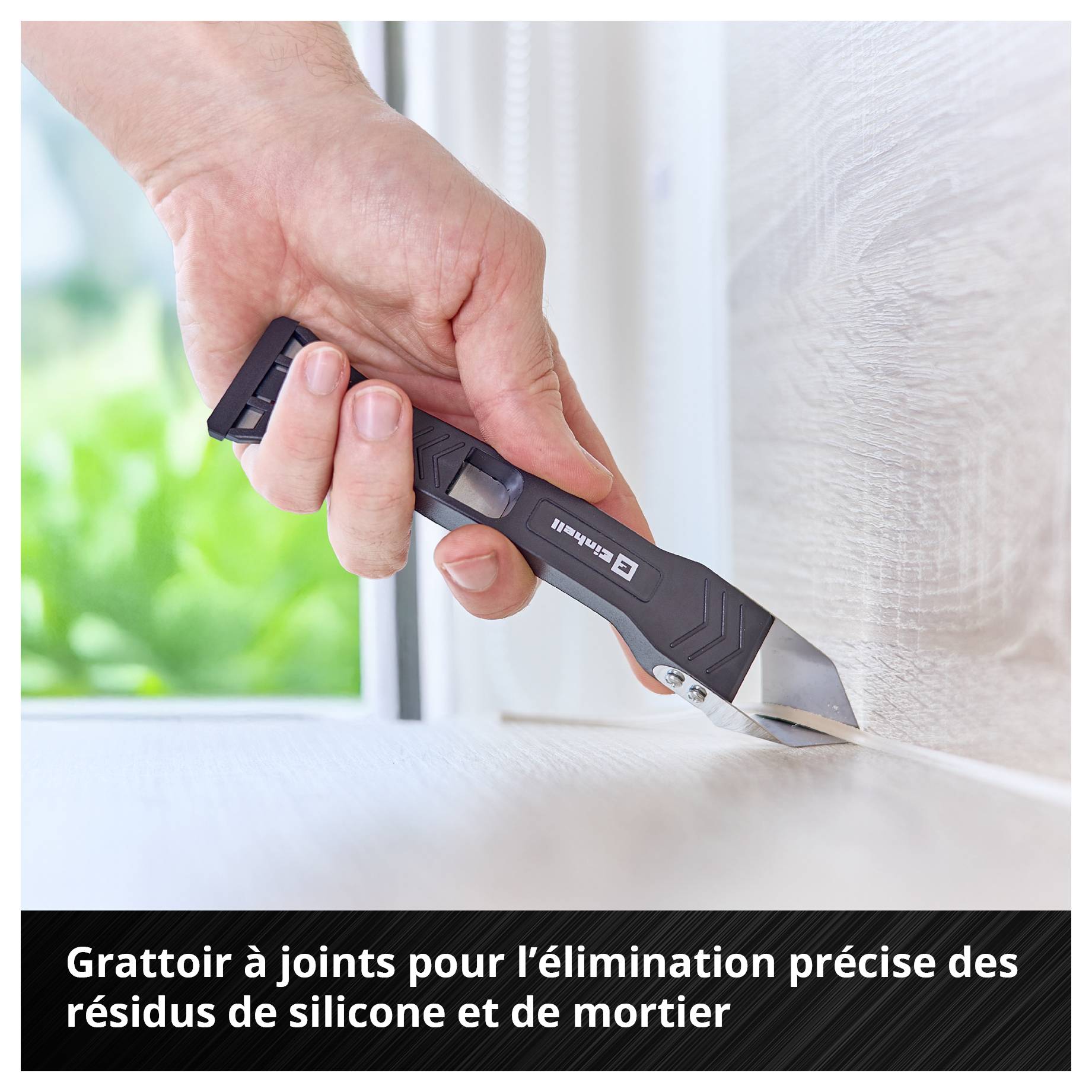 Main tenant un grattoir à joints et enlève les restes de silicone et de mortier d'une arête.