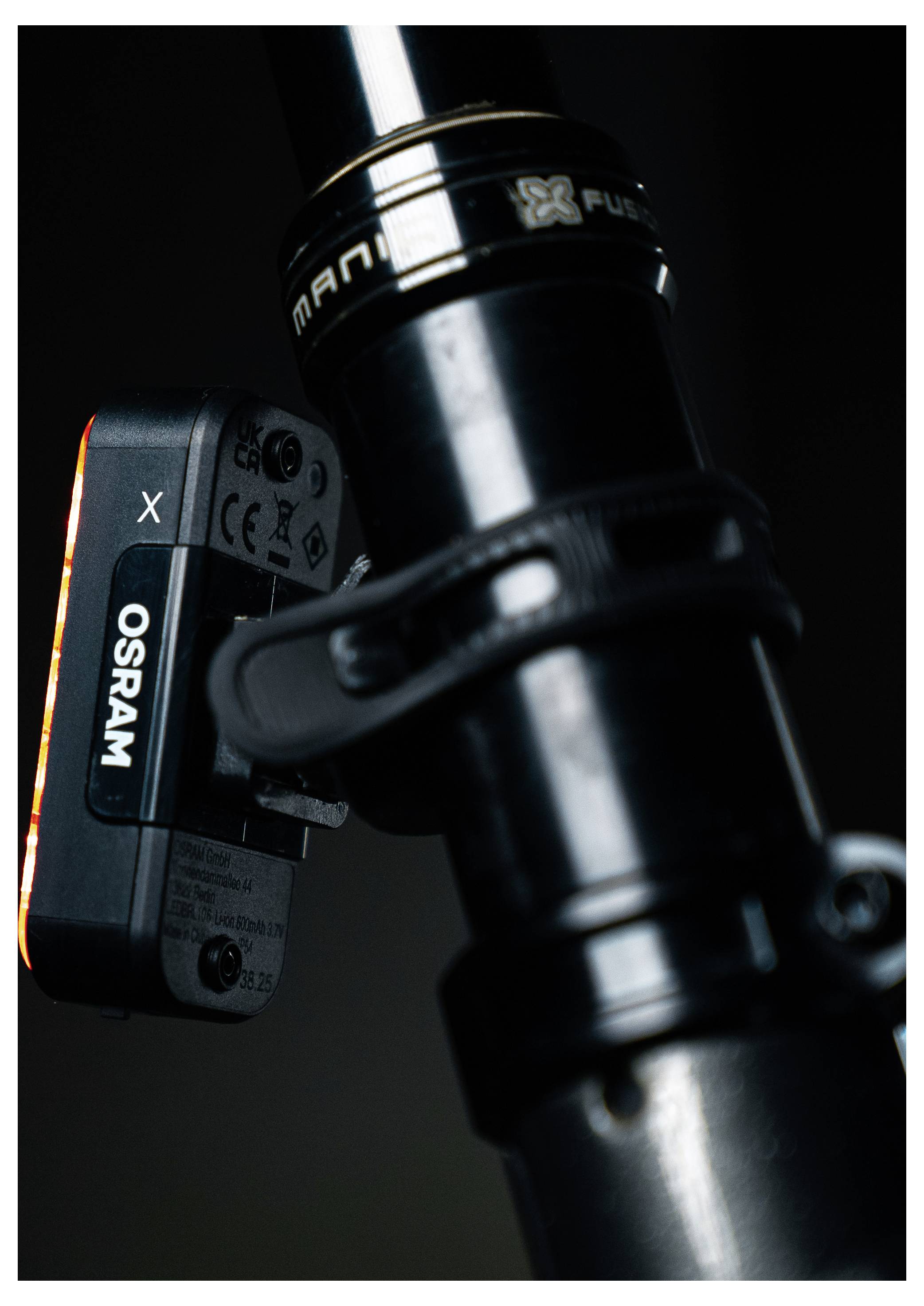 Un gros plan d'une tige de selle de vélo noire avec une lampe de vélo OSRAM attachée, fixée par une sangle, sur un fond sombre.
