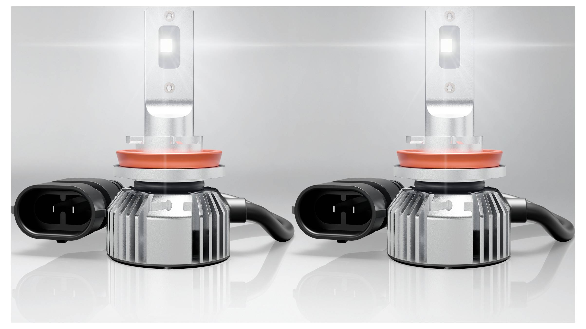 « Deux ampoules de phare LED avec des dissipateurs thermiques argentés et des connecteurs noirs, positionnées côte à côte sur une surface réfléchissante. »
