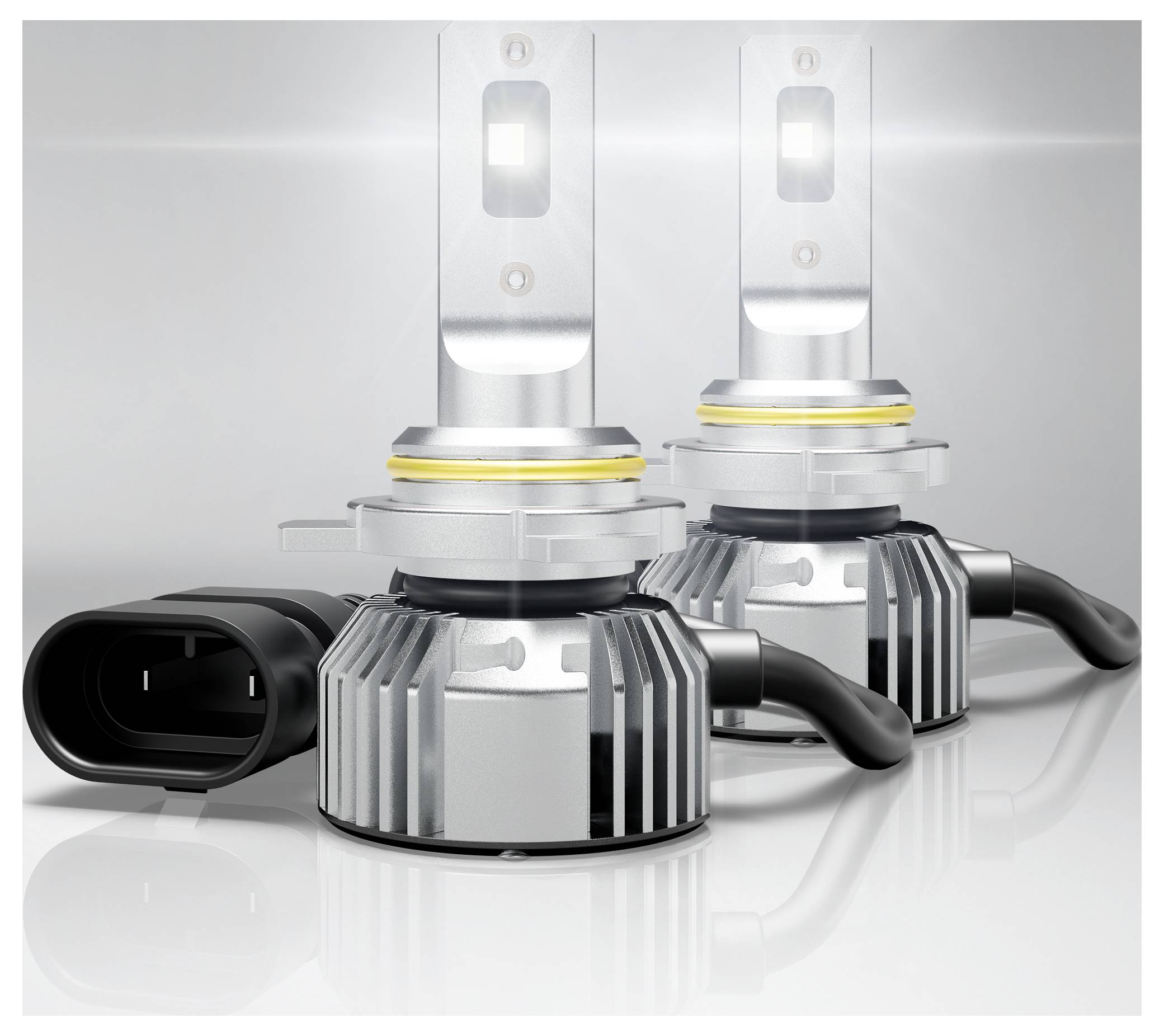 Deux ampoules de phare LED avec ailettes de refroidissement et connecteurs d'alimentation attachés sont positionnées sur une surface réfléchissante, mettant en évidence leur finition métallique.