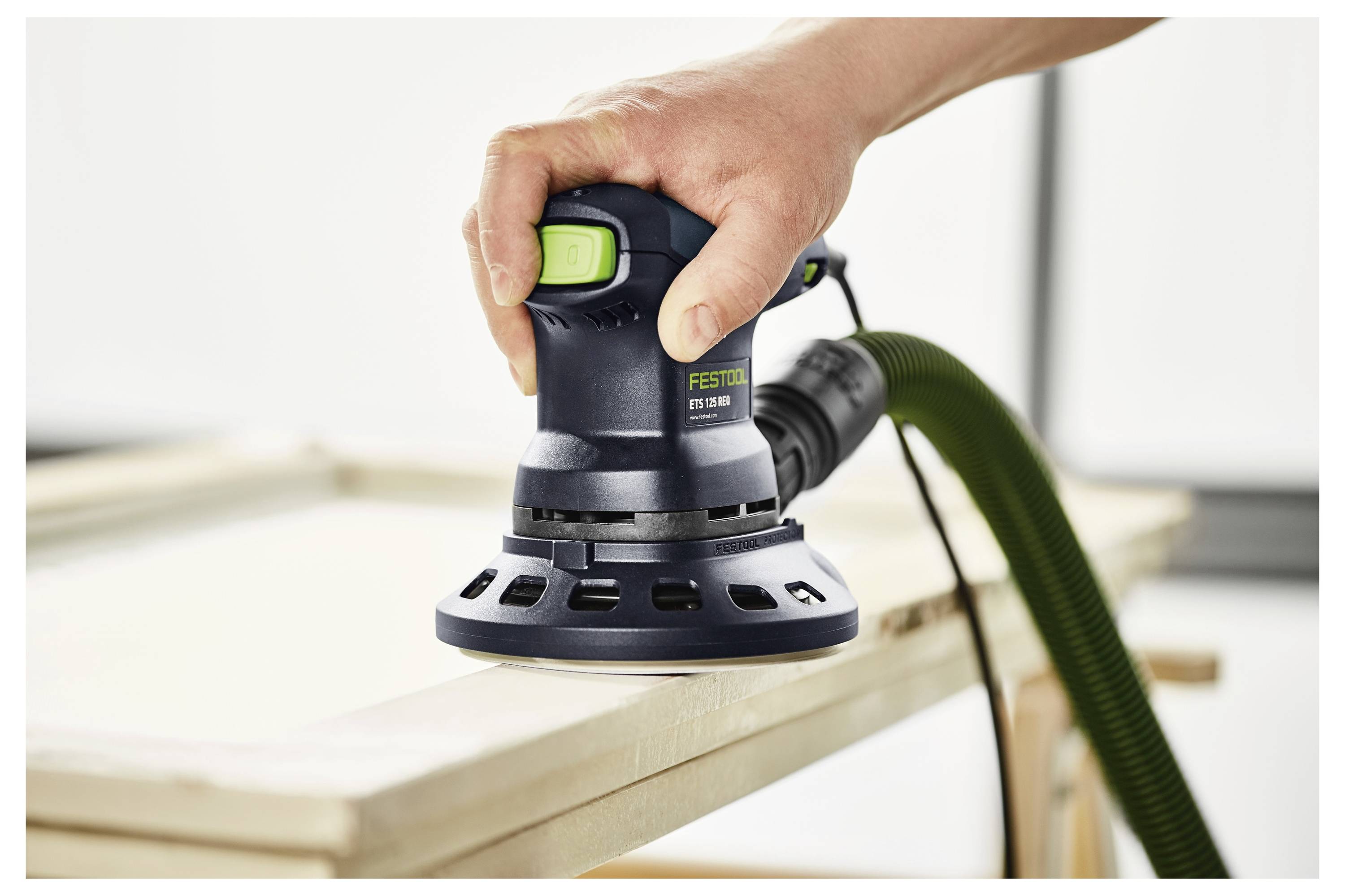 Une radio compacte Festool avec un affichage numérique et des boutons est posée sur un rebord de fenêtre donnant sur un chantier de construction extérieur flou.