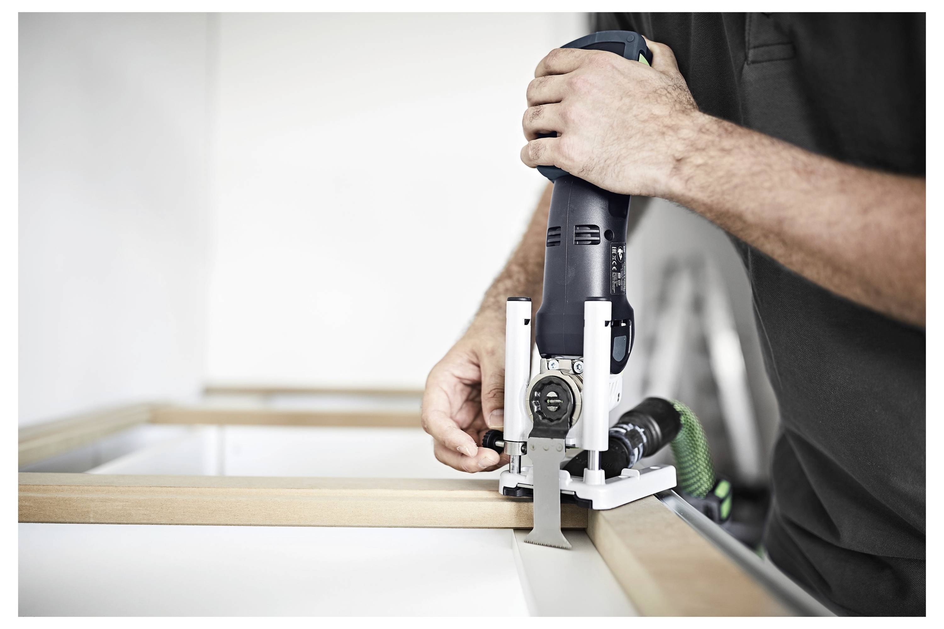 Une personne utilisant un outil portatif pour découper ou façonner un cadre en bois sur un établi. L'outil est électrique et conçu pour un travail de précision.