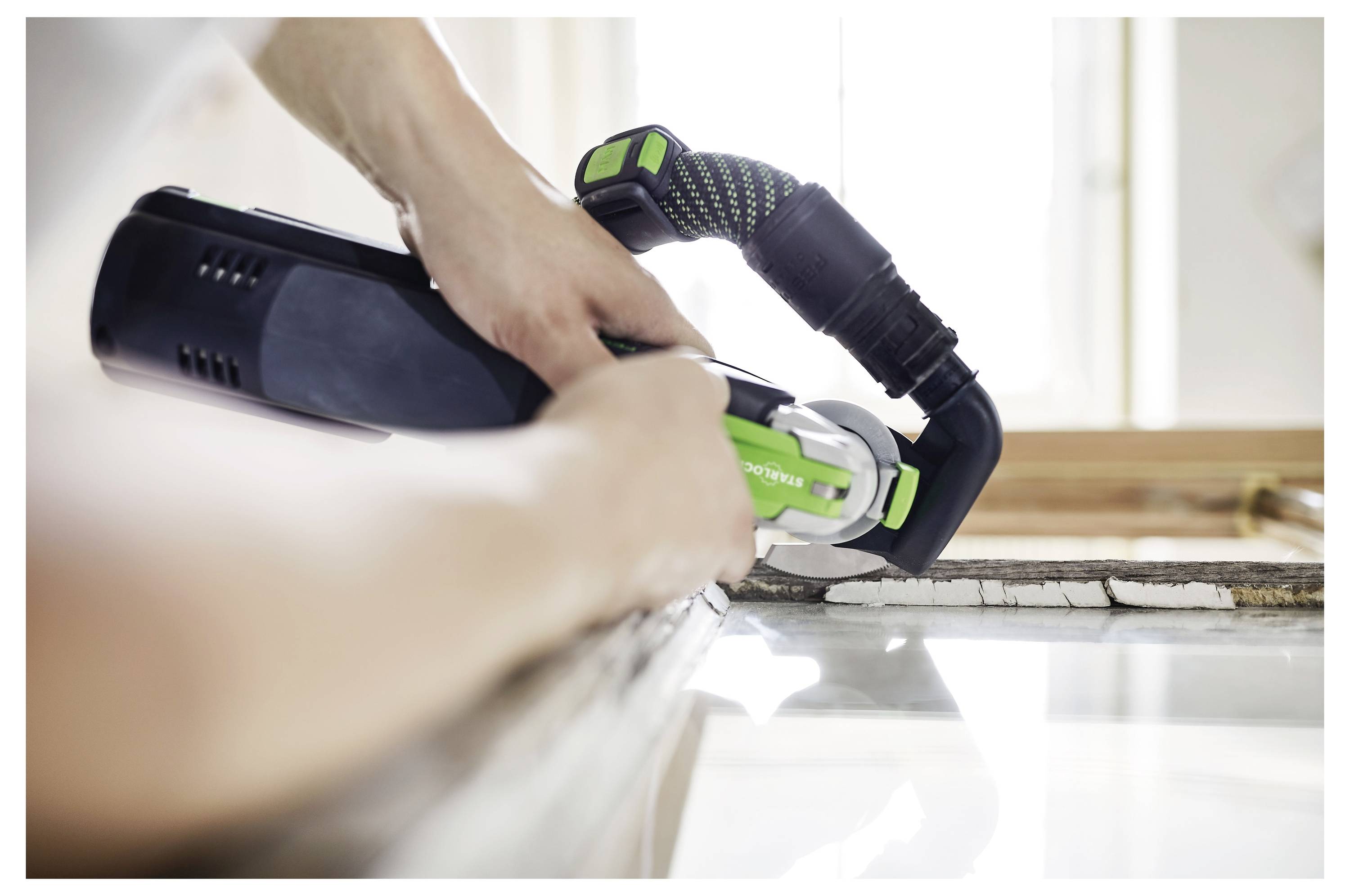 Une personne ajuste une ponceuse électrique dotée d'un plateau circulaire bleu, connectée à un extracteur de poussière Festool. Elle se prépare pour le ponçage.