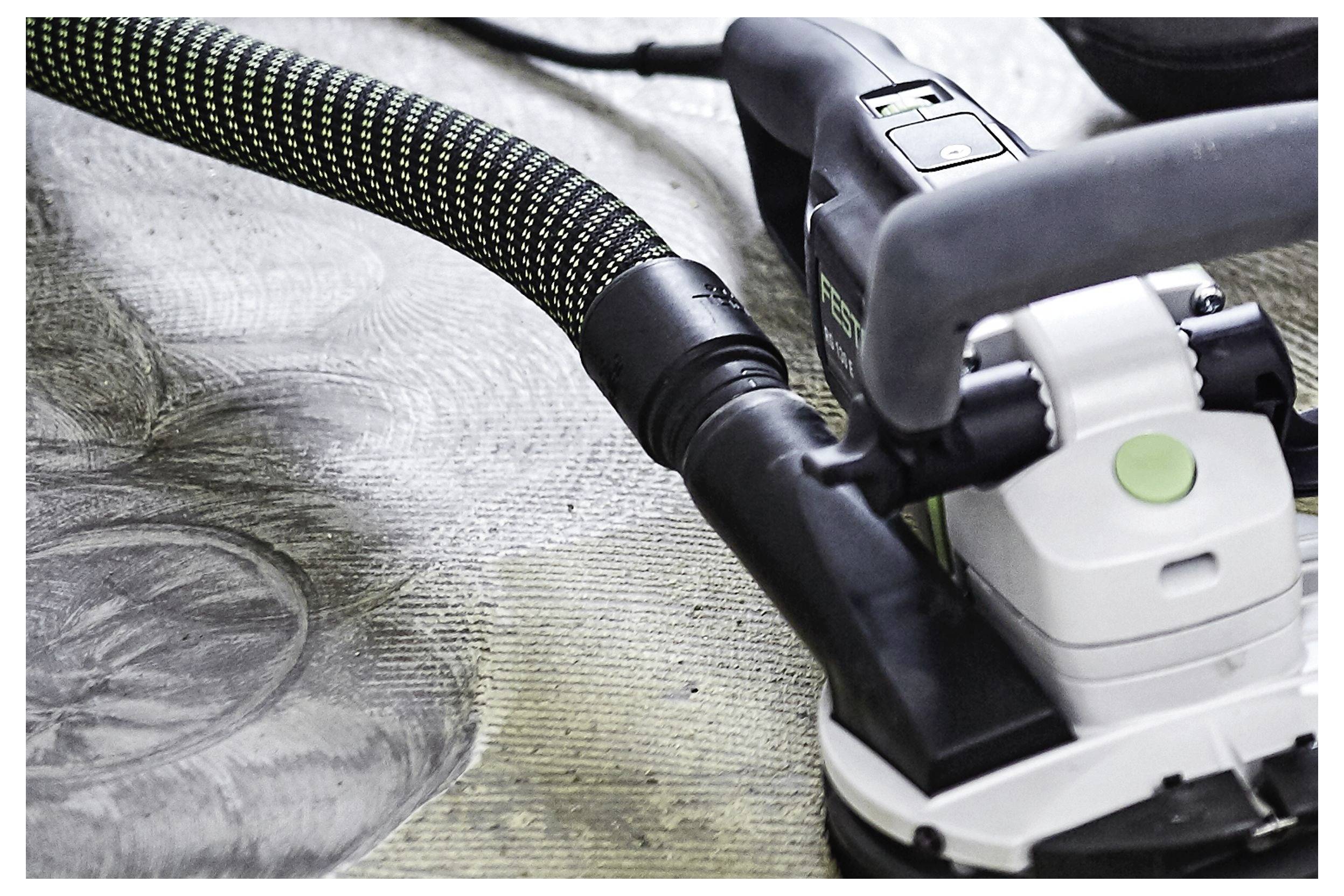 Un gros plan d'une ponceuse électrique avec un tuyau d'extraction de poussière attaché, lissant une surface en bois. Le grain et les motifs du bois sont visibles.