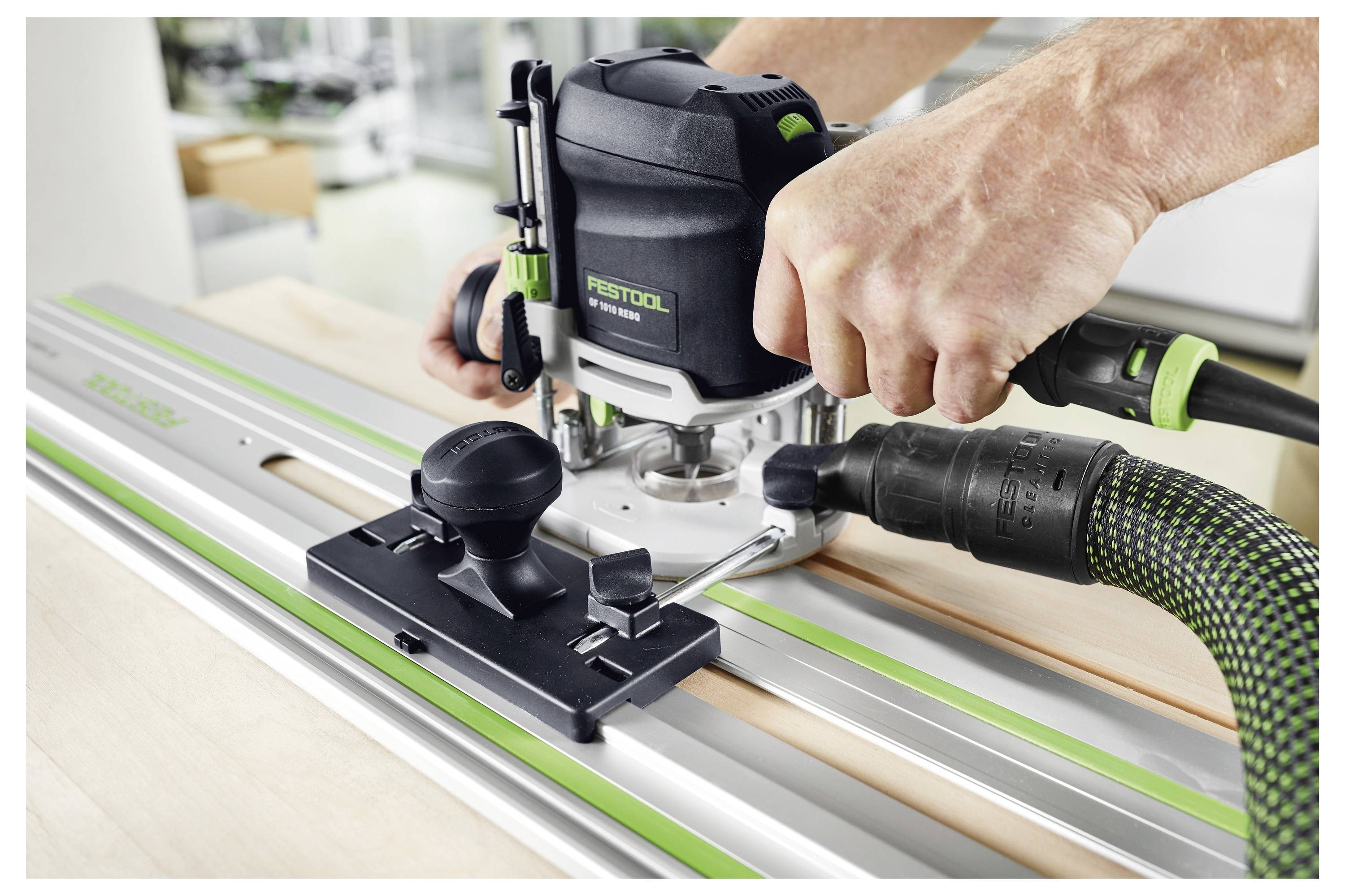 Une personne utilise une défonceuse Festool sur une surface en bois avec un rail de guidage. L'installation vise à réaliser une découpe de bois précise, en mettant l'accent sur la sécurité des outils et le contrôle.