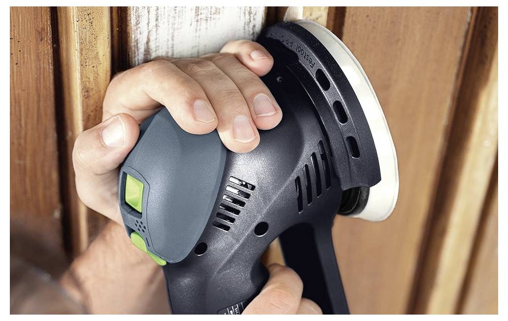 La main d'une personne utilise une ponceuse électrique sur une surface en bois, lissant le matériau avec précision et soin.