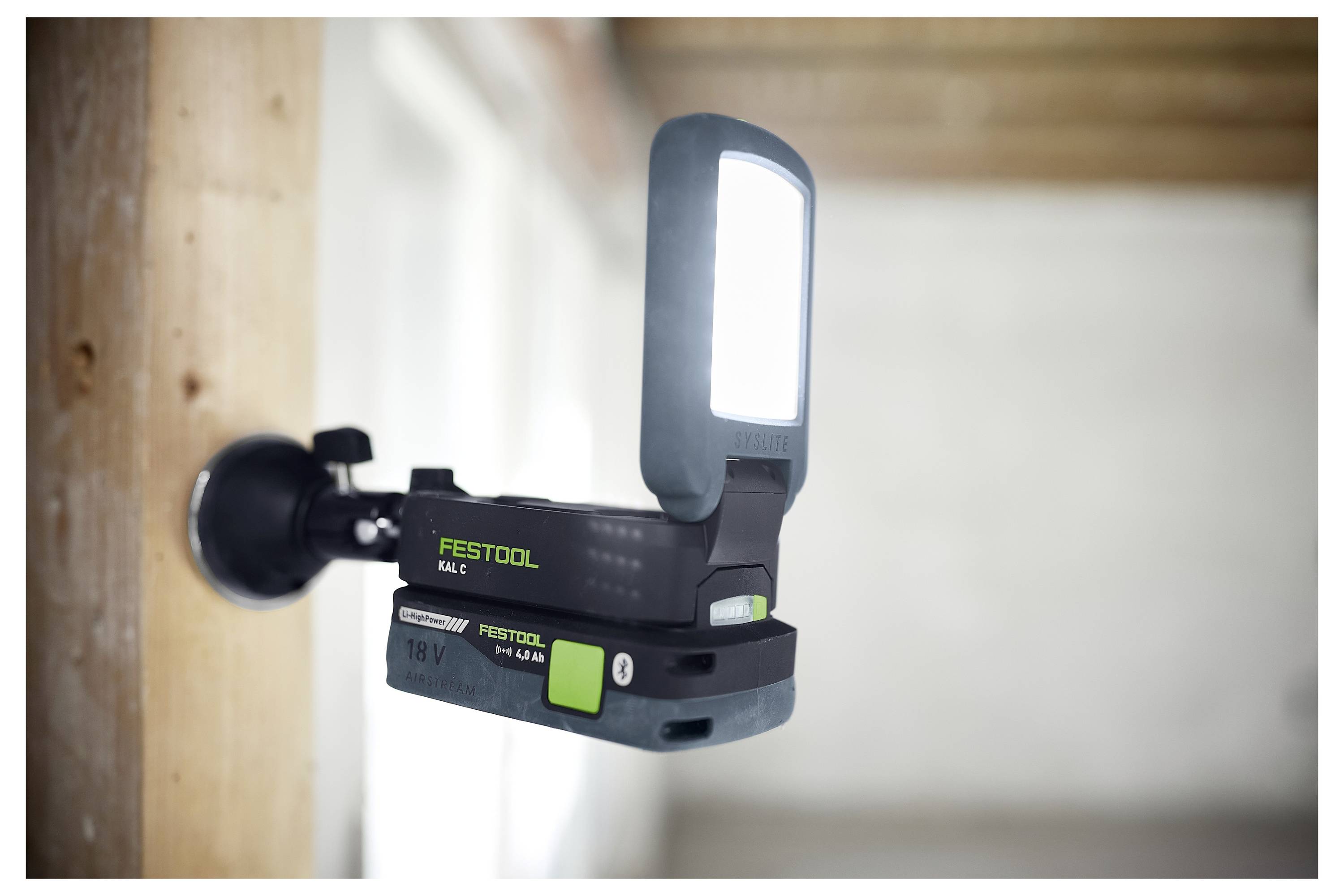 A mounted, illuminated work light is attached to a wooden beam in a construction setting, providing focused lighting for tasks.