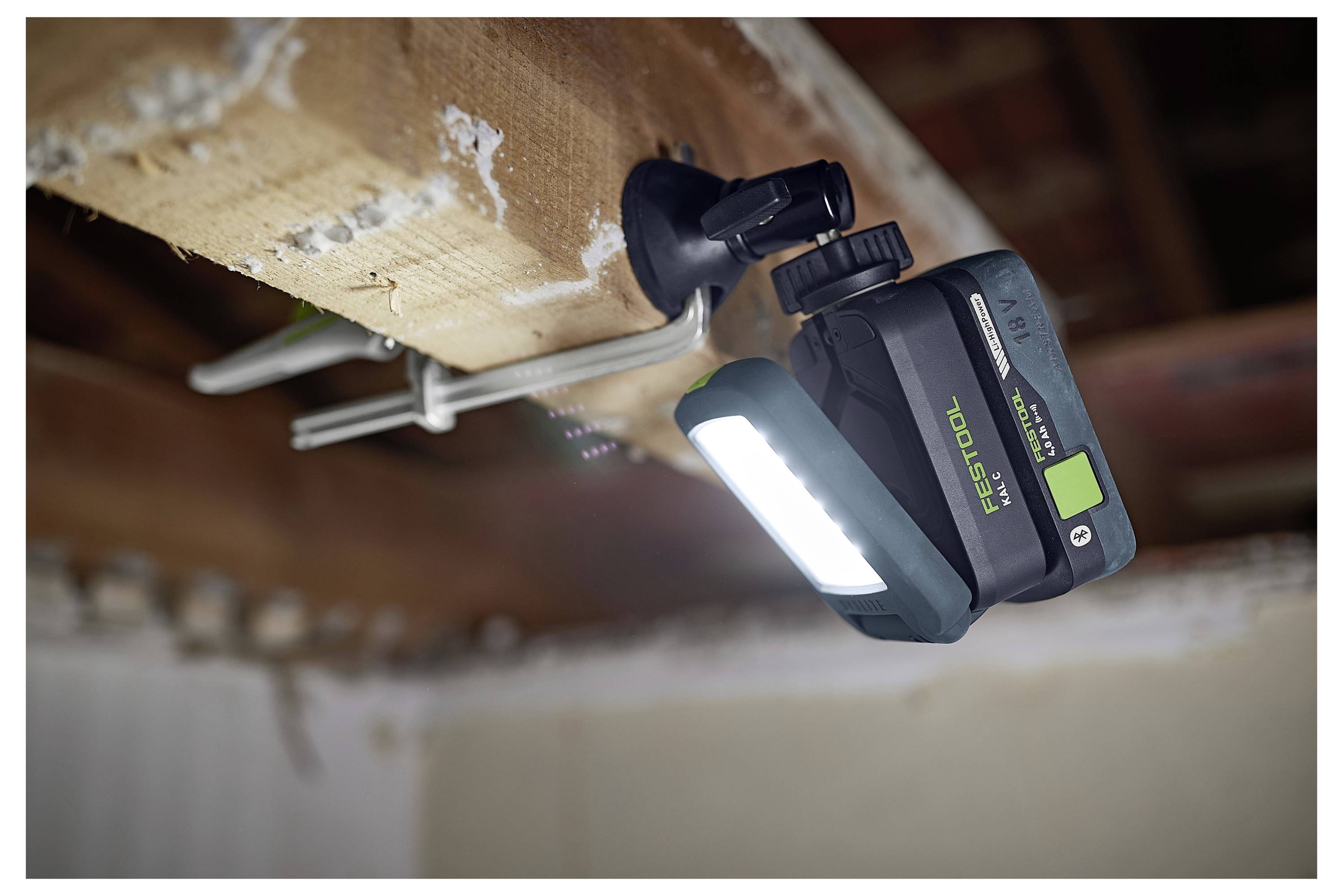 Une lampe de travail LED portable fixée à une poutre en bois, illuminant un espace de travail. Convient pour une utilisation sans les mains dans les tâches de construction ou de réparation.