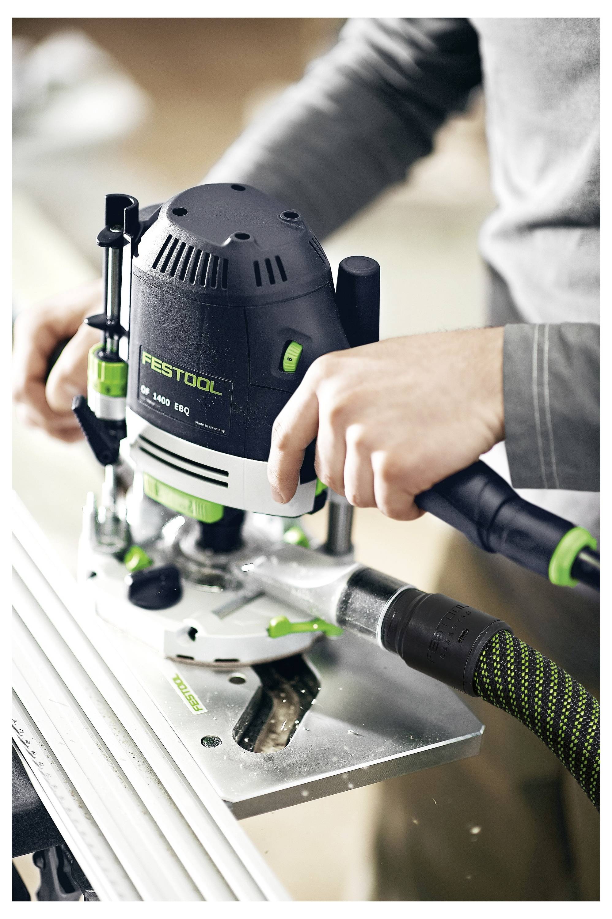 Une personne utilise une défonceuse Festool pour découper une rainure dans une tôle métallique, en mettant l'accent sur la précision et le contrôle avec un tuyau d'aspiration attaché.
