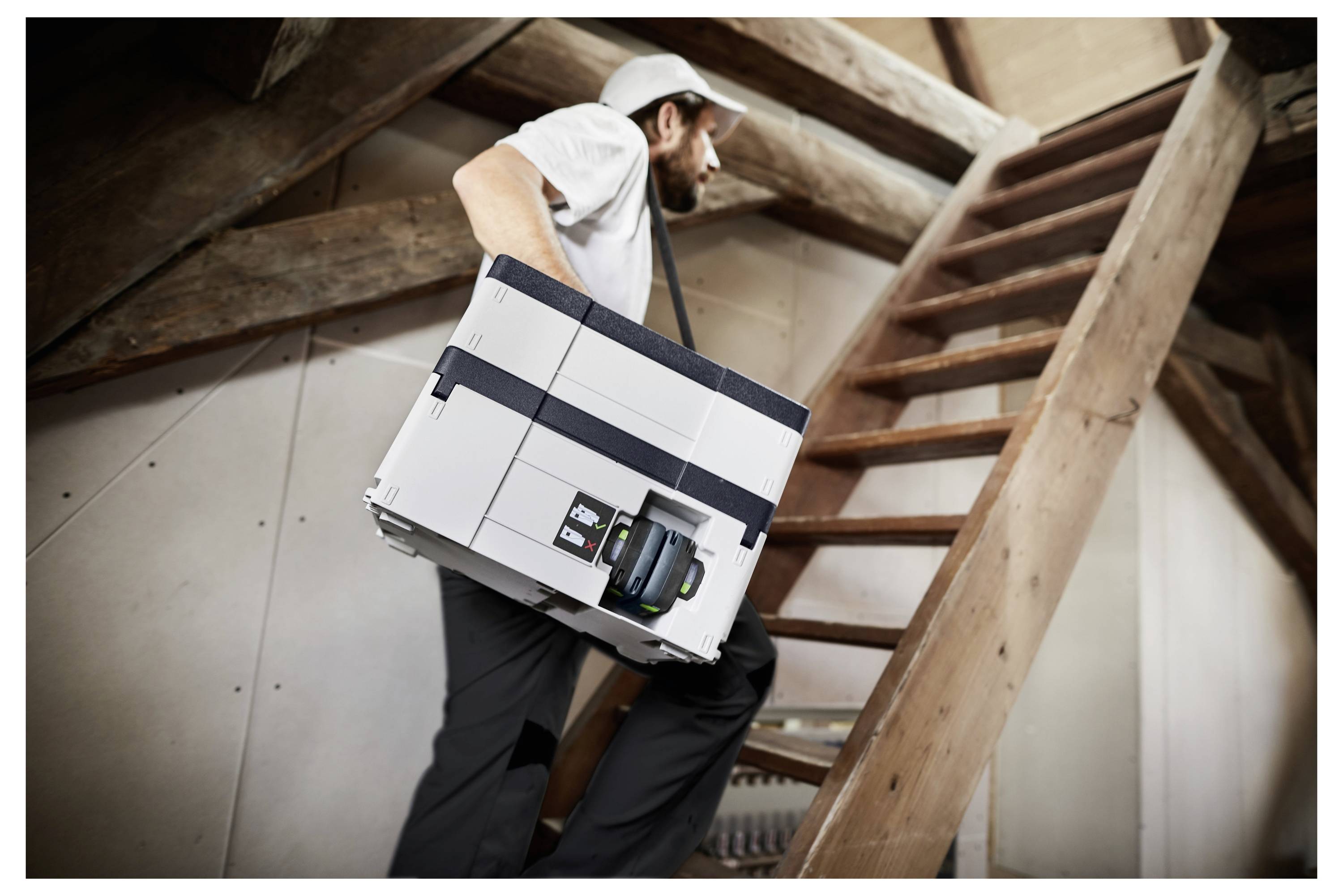 Une personne porte un grand objet de forme rectangulaire dans un escalier en bois dans un cadre rustique, ce qui suggère du mouvement et un effort physique.