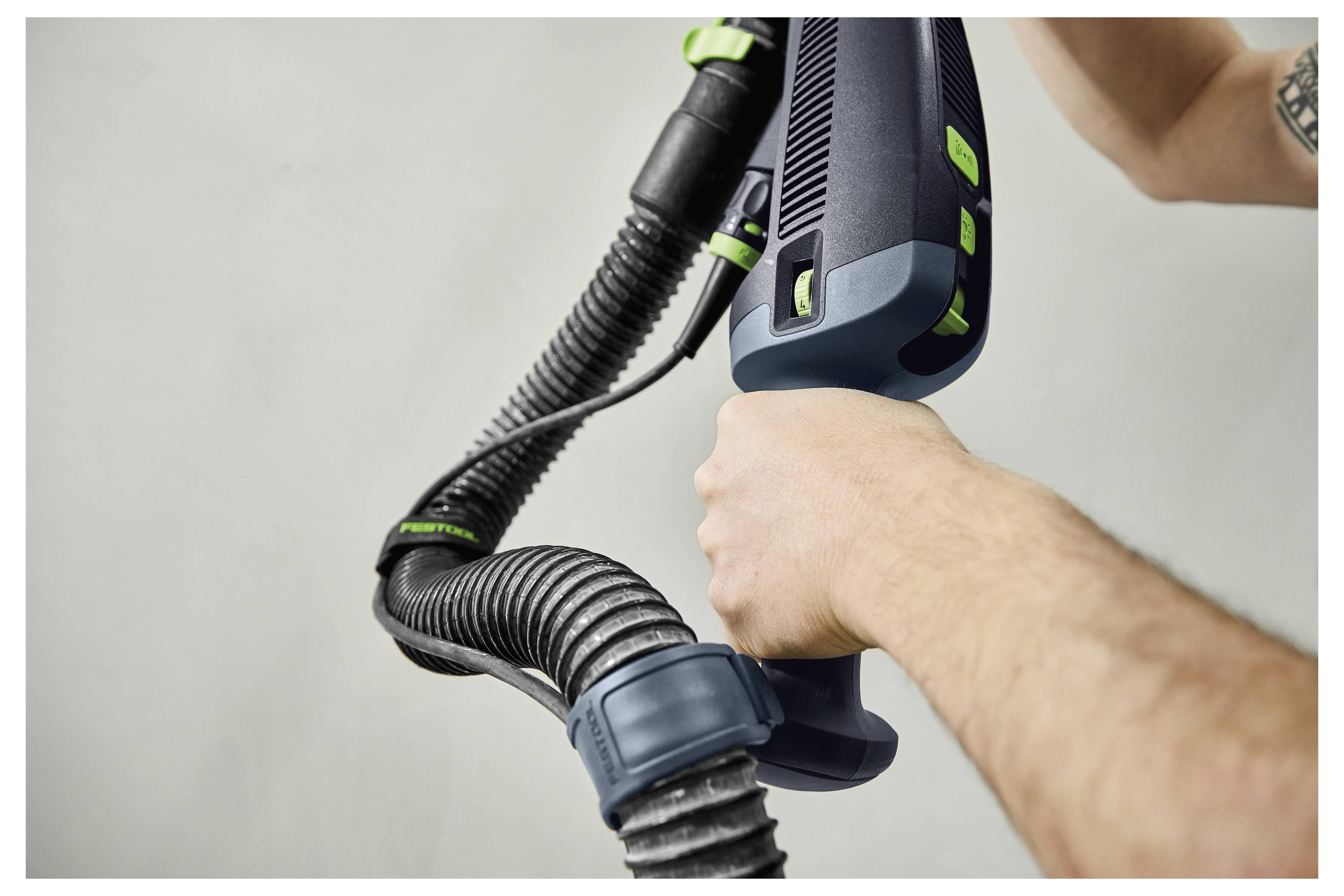 Mains tenant une buse d'aspirateur et un tuyau, avec un accent sur la prise et la maniabilité, sur un fond uni.