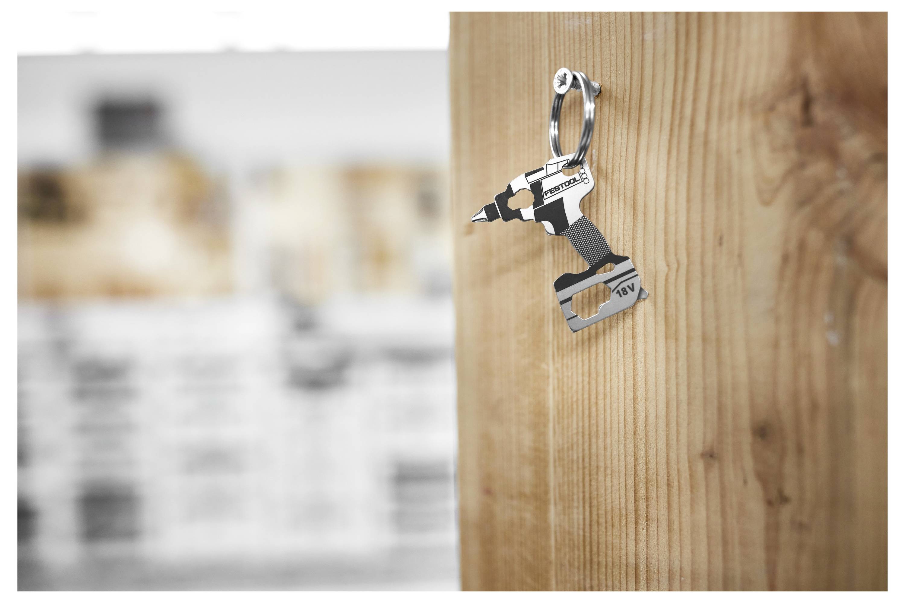 Un porte-clés en forme de perceuse sans fil pend sur un mur en bois. L'arrière-plan est flou, mettant l'accent sur le porte-clés au thème d'outils original et farfelu.