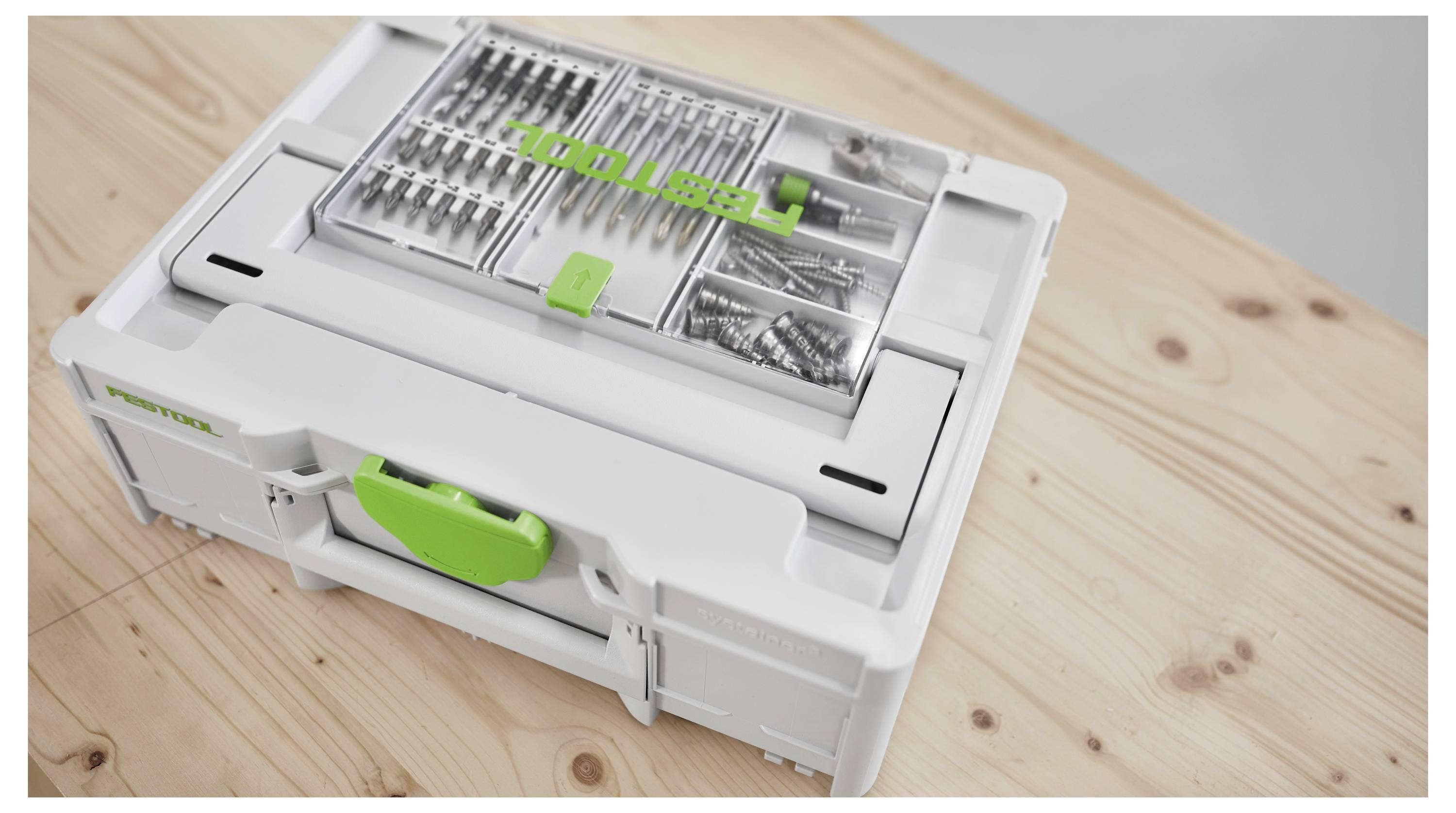 Une boîte à outils Festool blanche sur une surface en bois, contenant des forets et des vis soigneusement organisés à l'intérieur d'un couvercle à compartiment transparent.