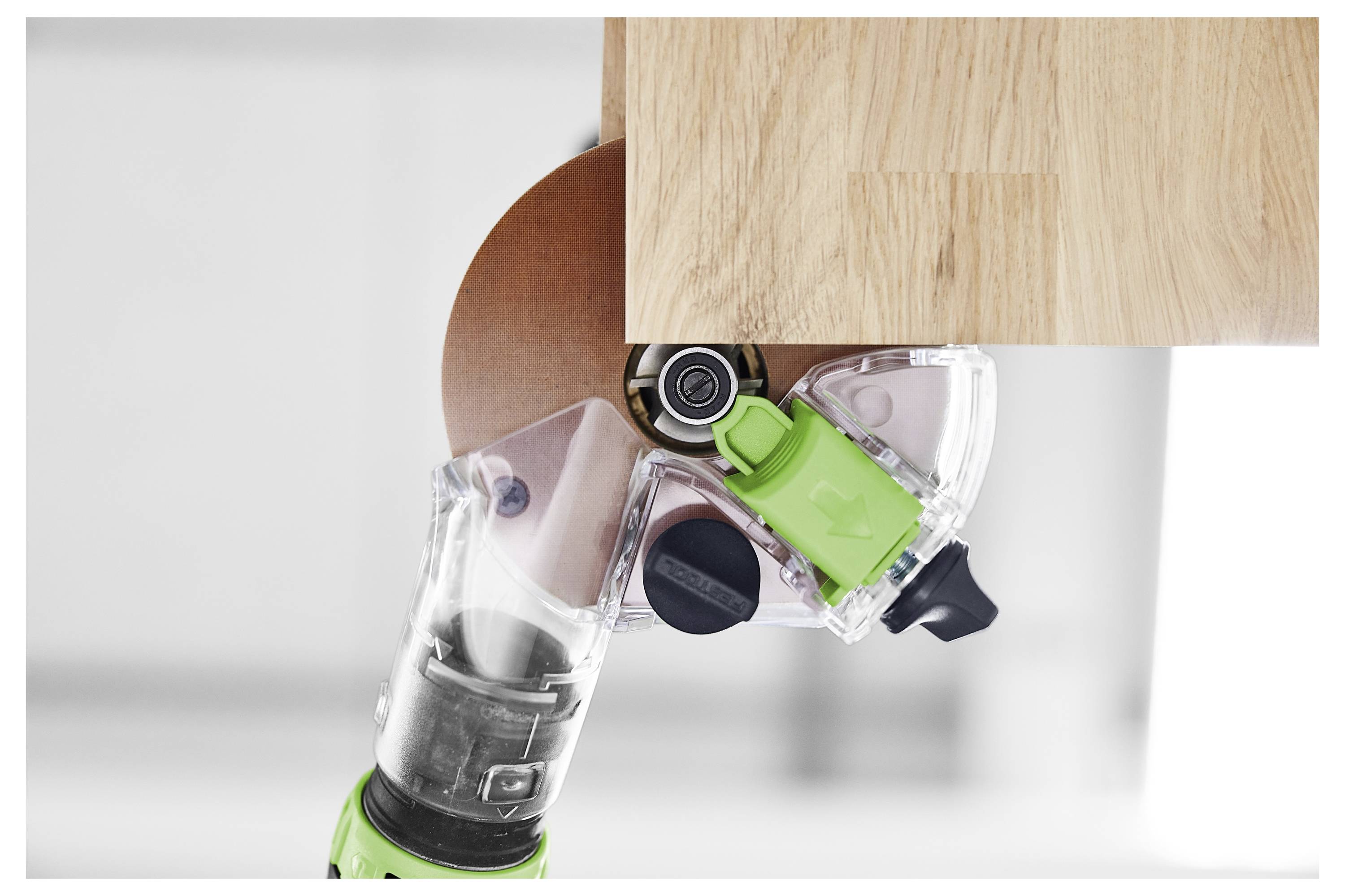A close-up of a power tool with a circular cutting blade trimming the edge of a wooden surface. The tool features a green handle.