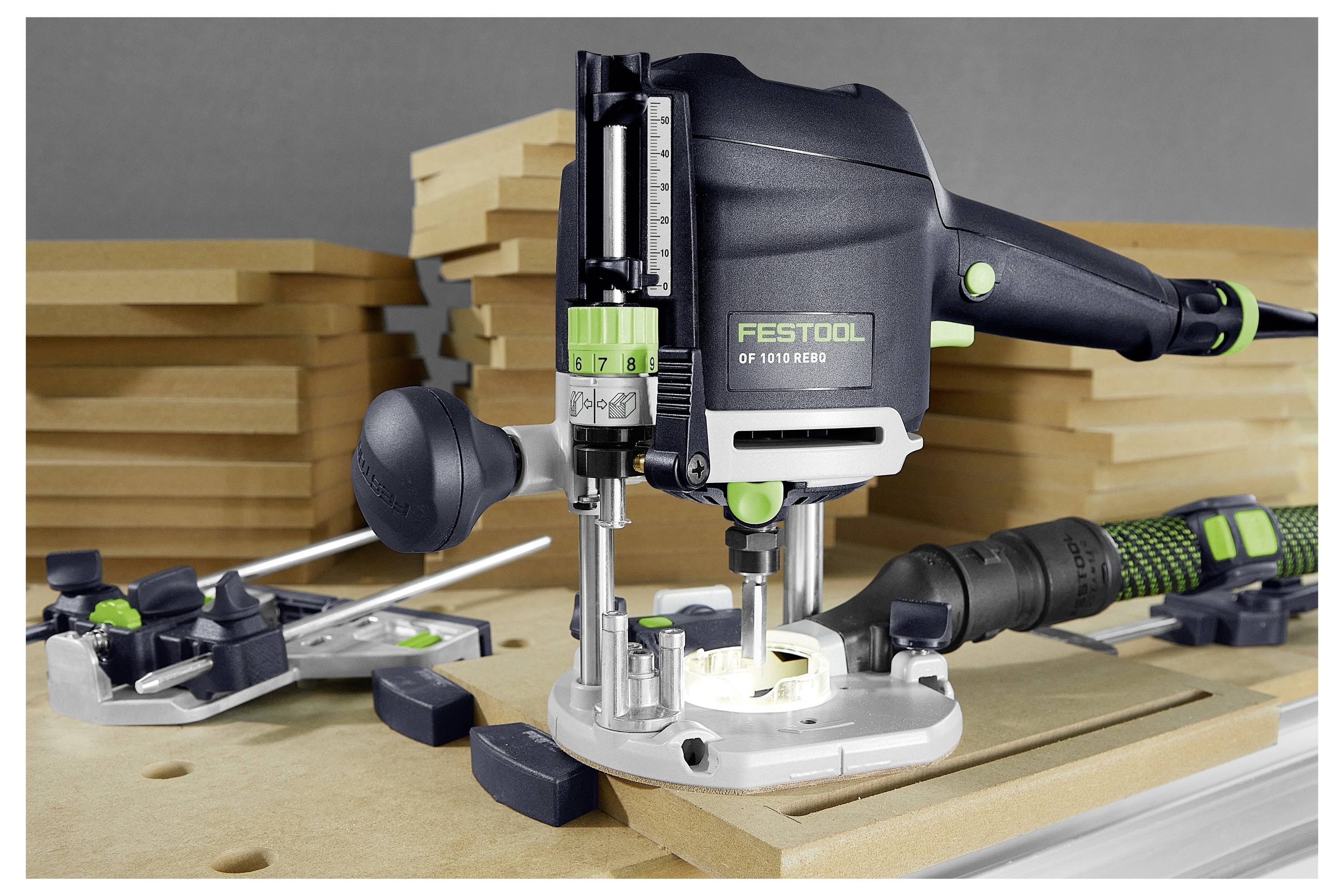 Un routeur Festool noir et vert sur un établi, entouré de pièces de bois et d'une fixation de rail de guidage, utilisé pour le travail du bois de précision.