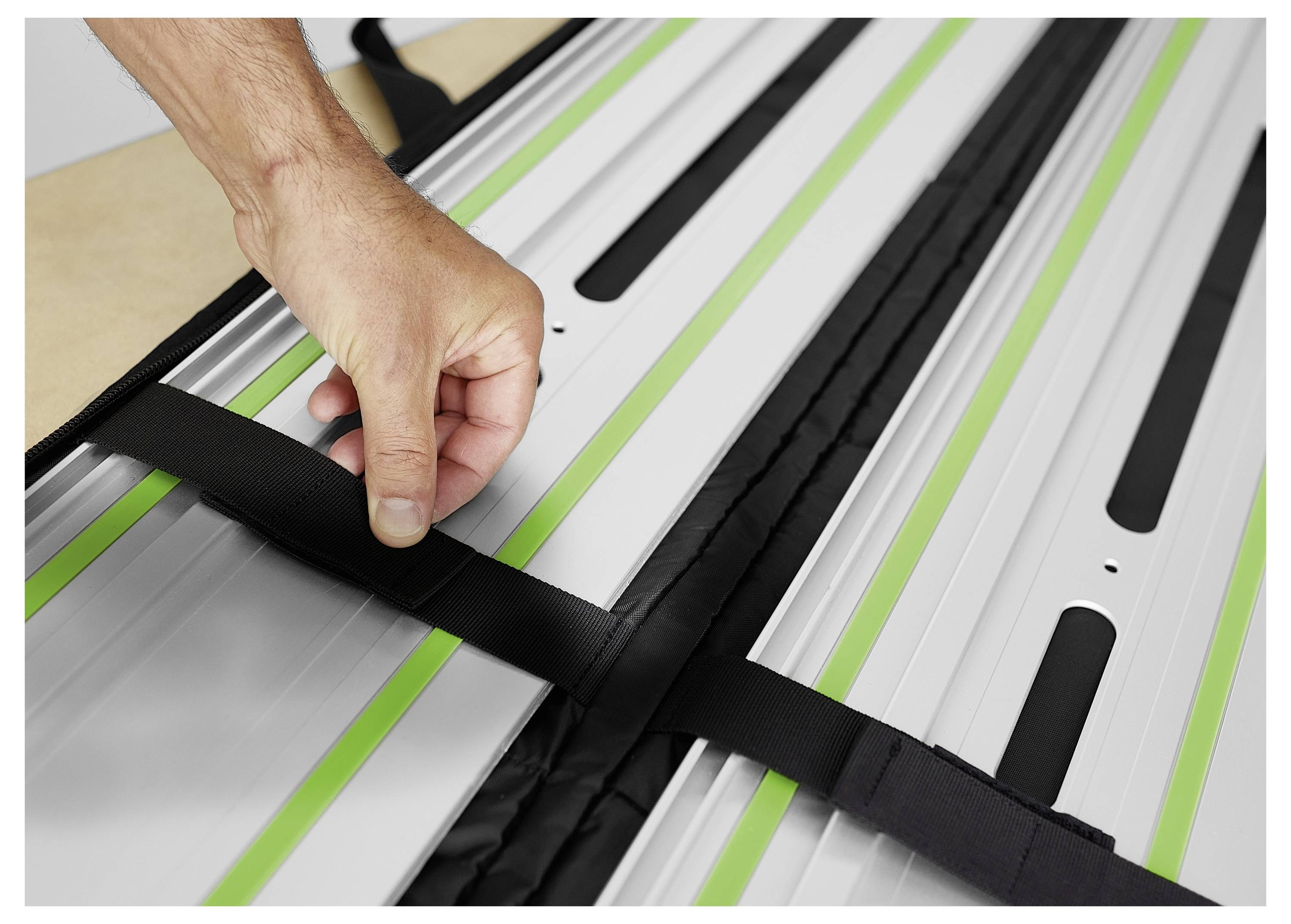 Une main ajuste des sangles noires sur une surface métallique avec des lignes vertes, probablement pour sécuriser l'équipement avant utilisation.