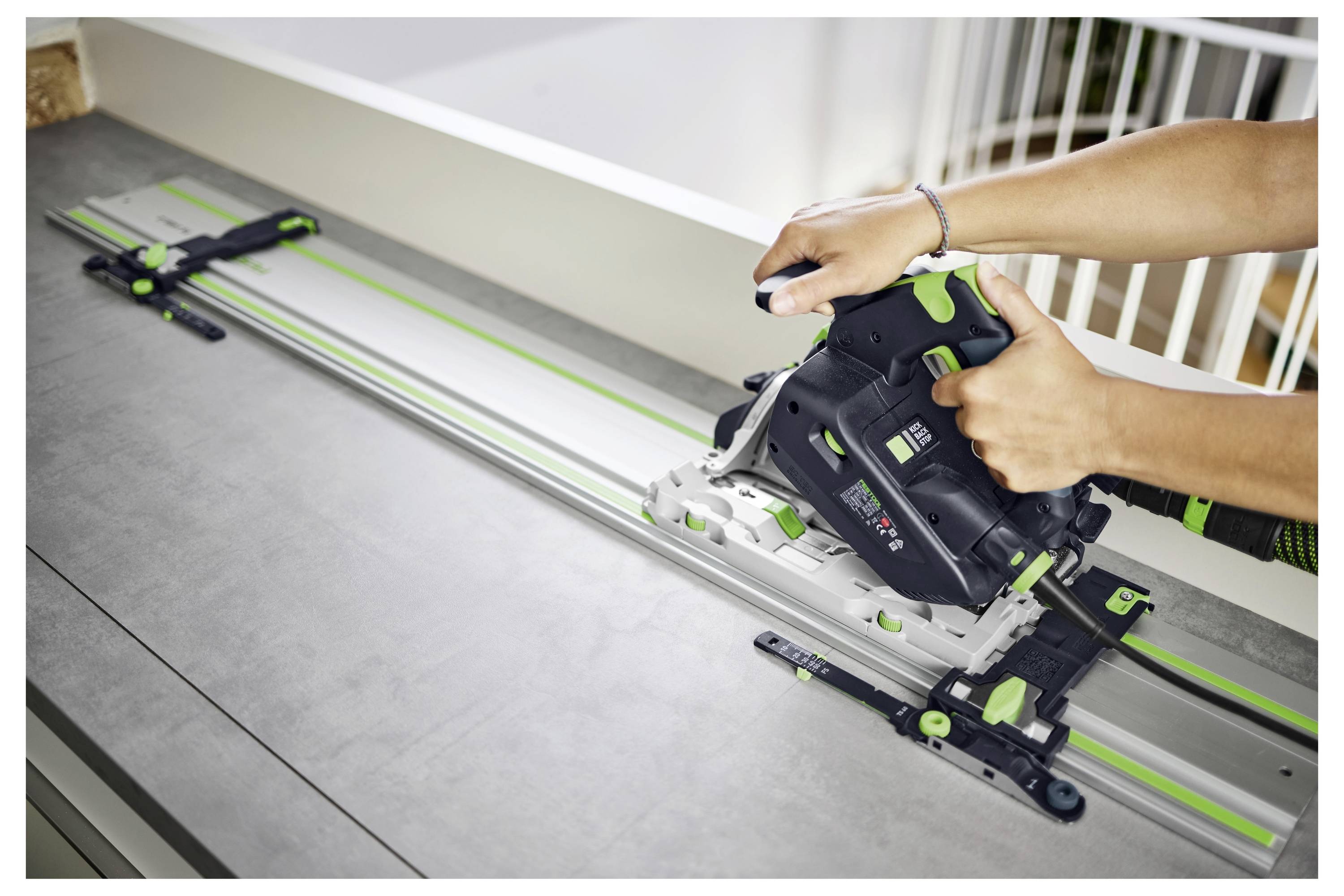Une personne utilise une scie électrique portative sur un rail de guidage métallique pour effectuer une coupe précise sur une surface plane à l'intérieur.