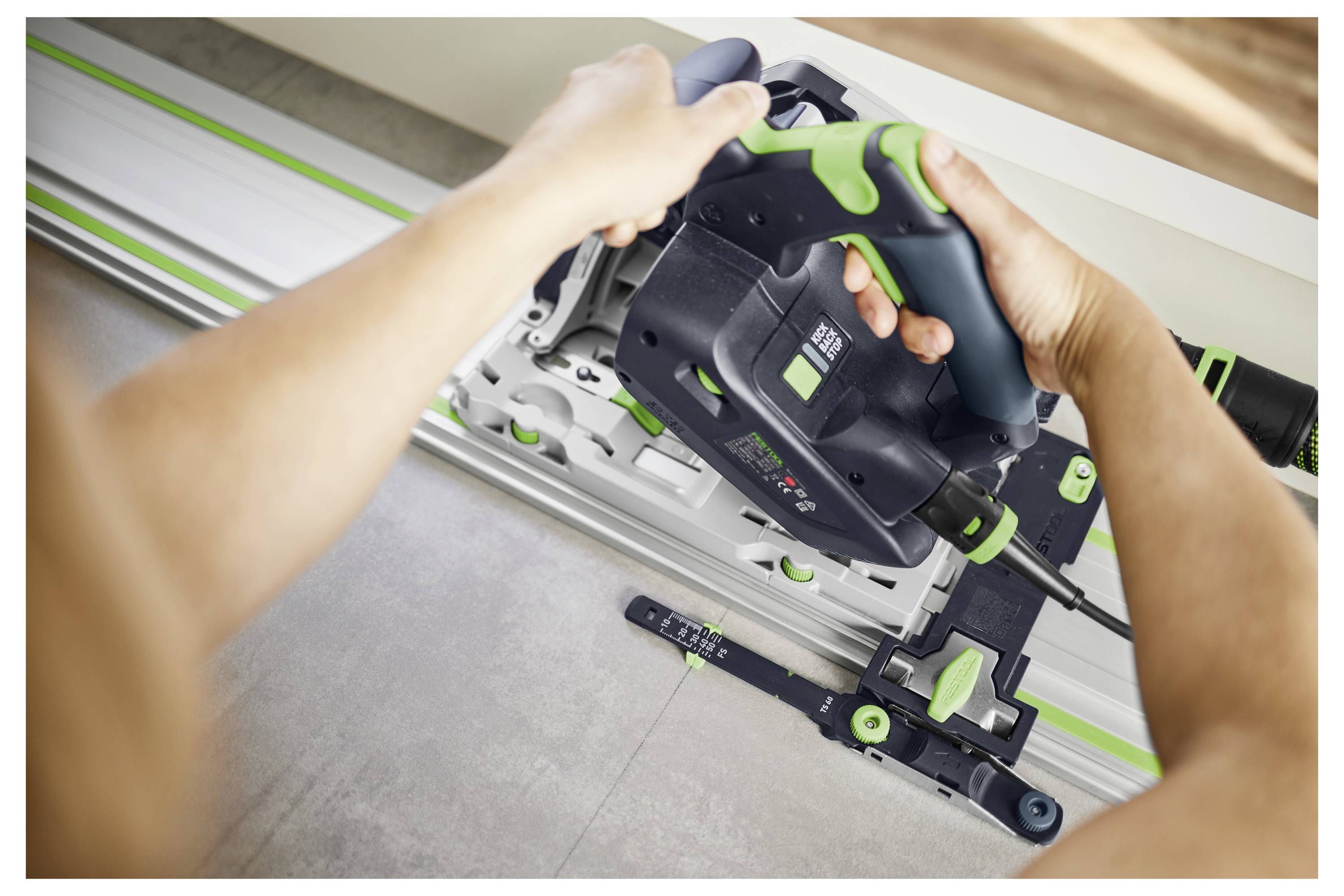 Person using a circular saw on a metal track to cut a material, likely wood or laminate, with a focus on precision and control.