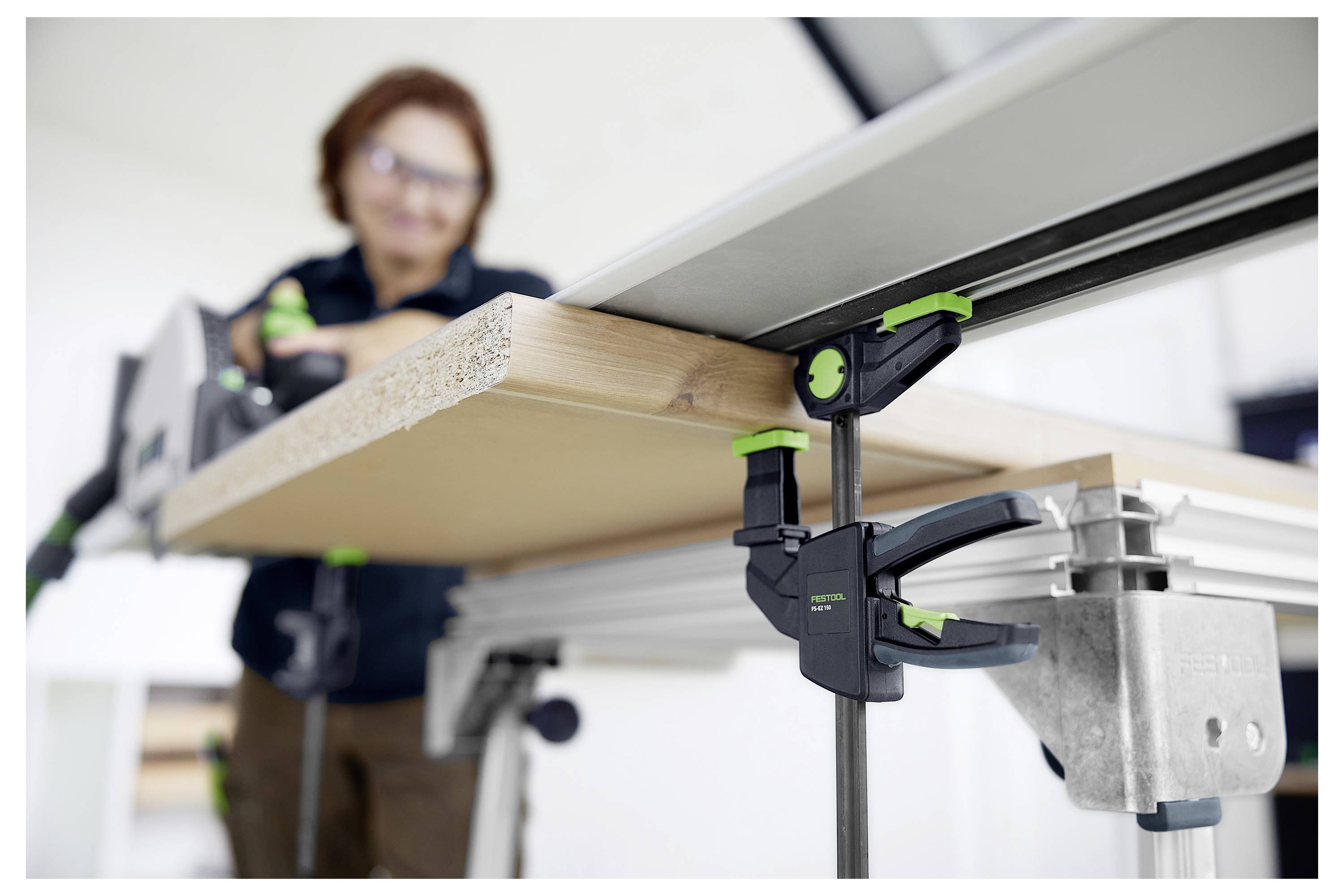 Une personne utilise des serre-joints verts et noirs pour fixer une planche en bois à une scie à table, en mettant l'accent sur le travail du bois de précision.
