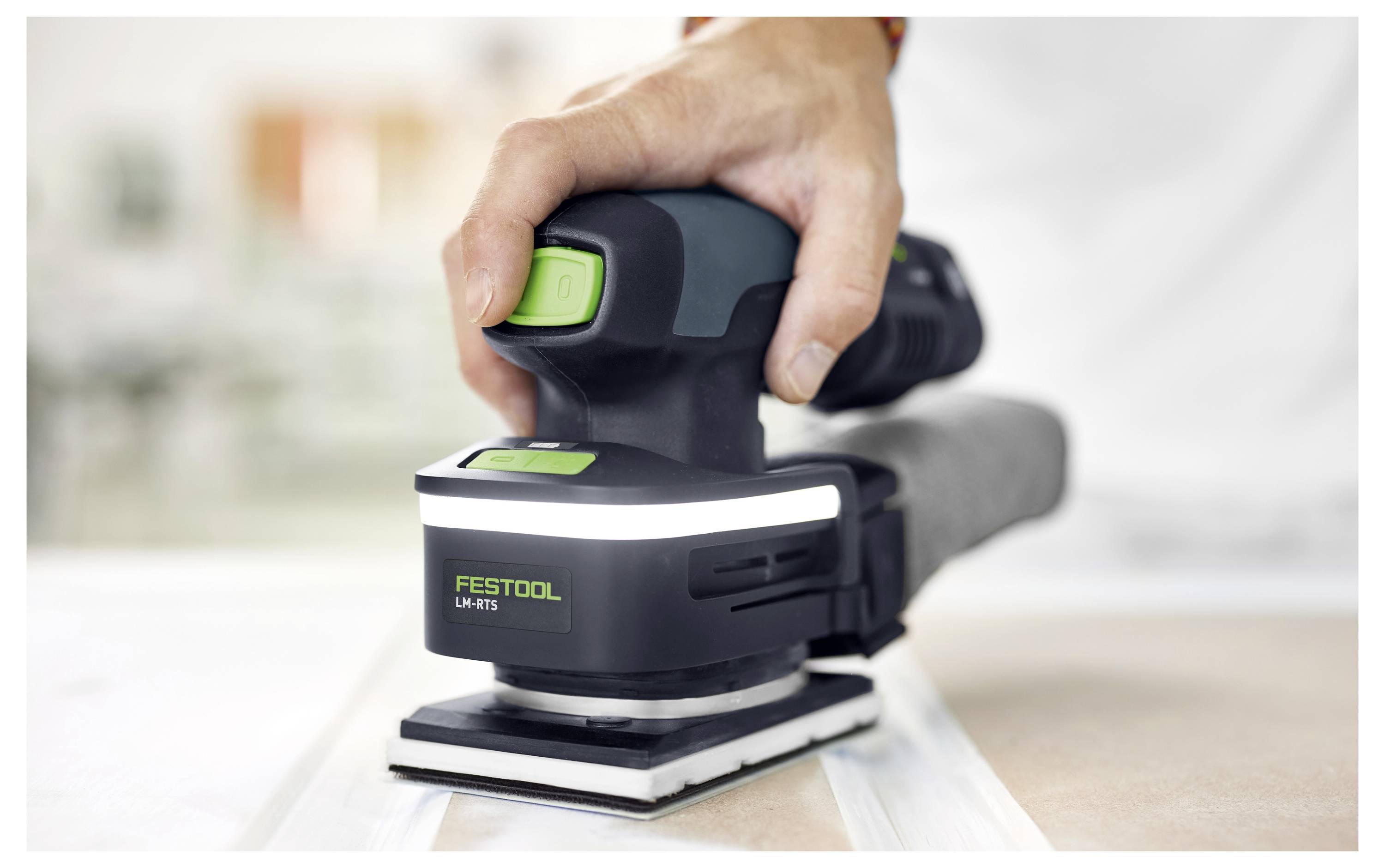 Une main utilisant un ponceuse Festool sur une surface plane, mettant en avant sa conception ergonomique et ses caractéristiques de contrôle, soulignant la précision dans les tâches de ponçage.