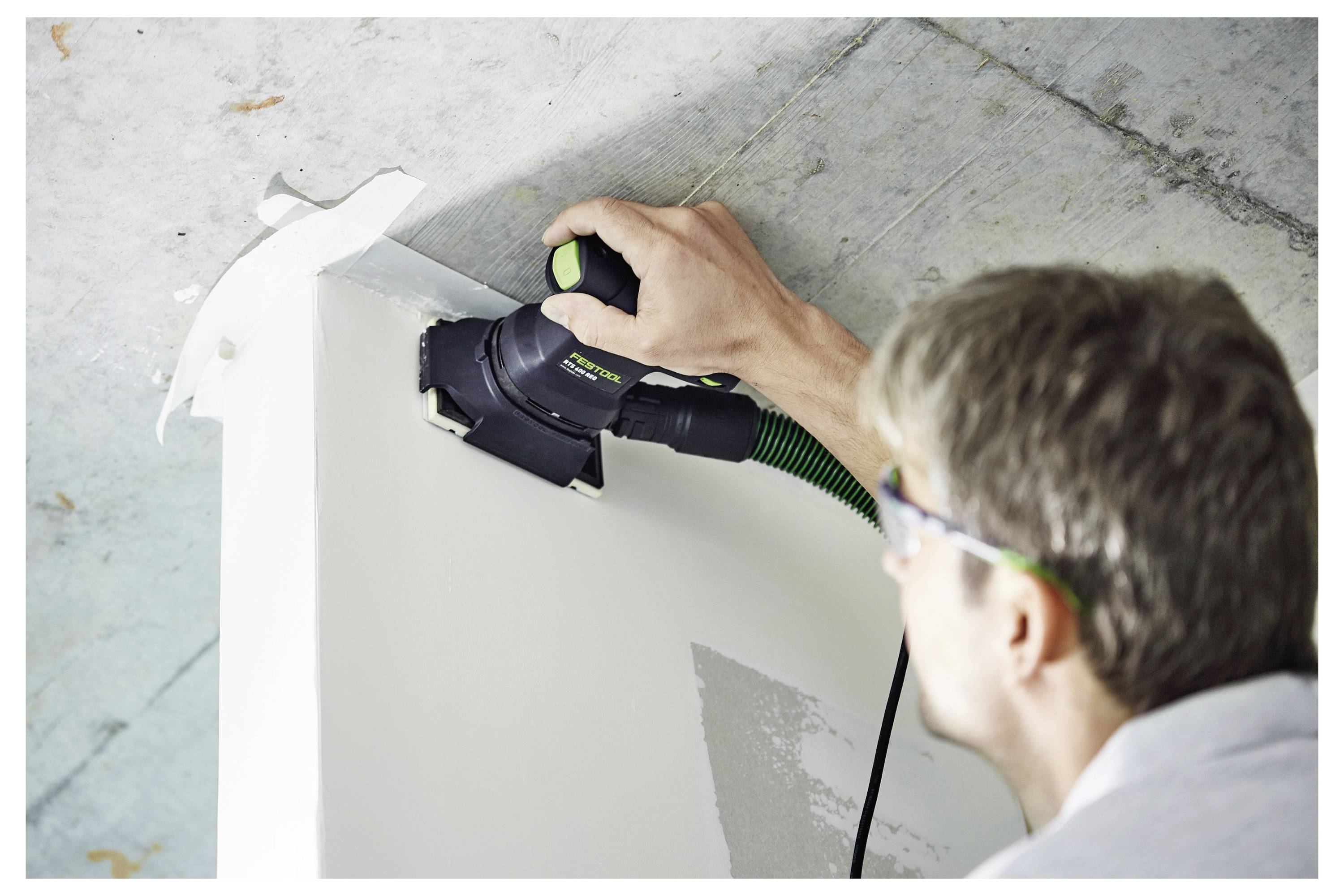 A person sanding a wall corner using an electric sander, focusing on precise, smooth finishing for home renovation or construction work.