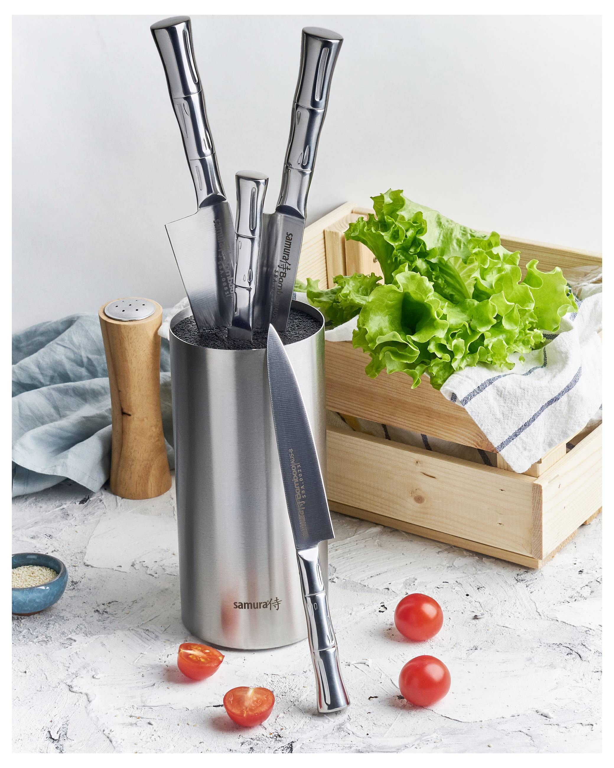 A set of three knives in a metal holder with tomatoes and lettuce beside a wooden crate, on a kitchen counter.