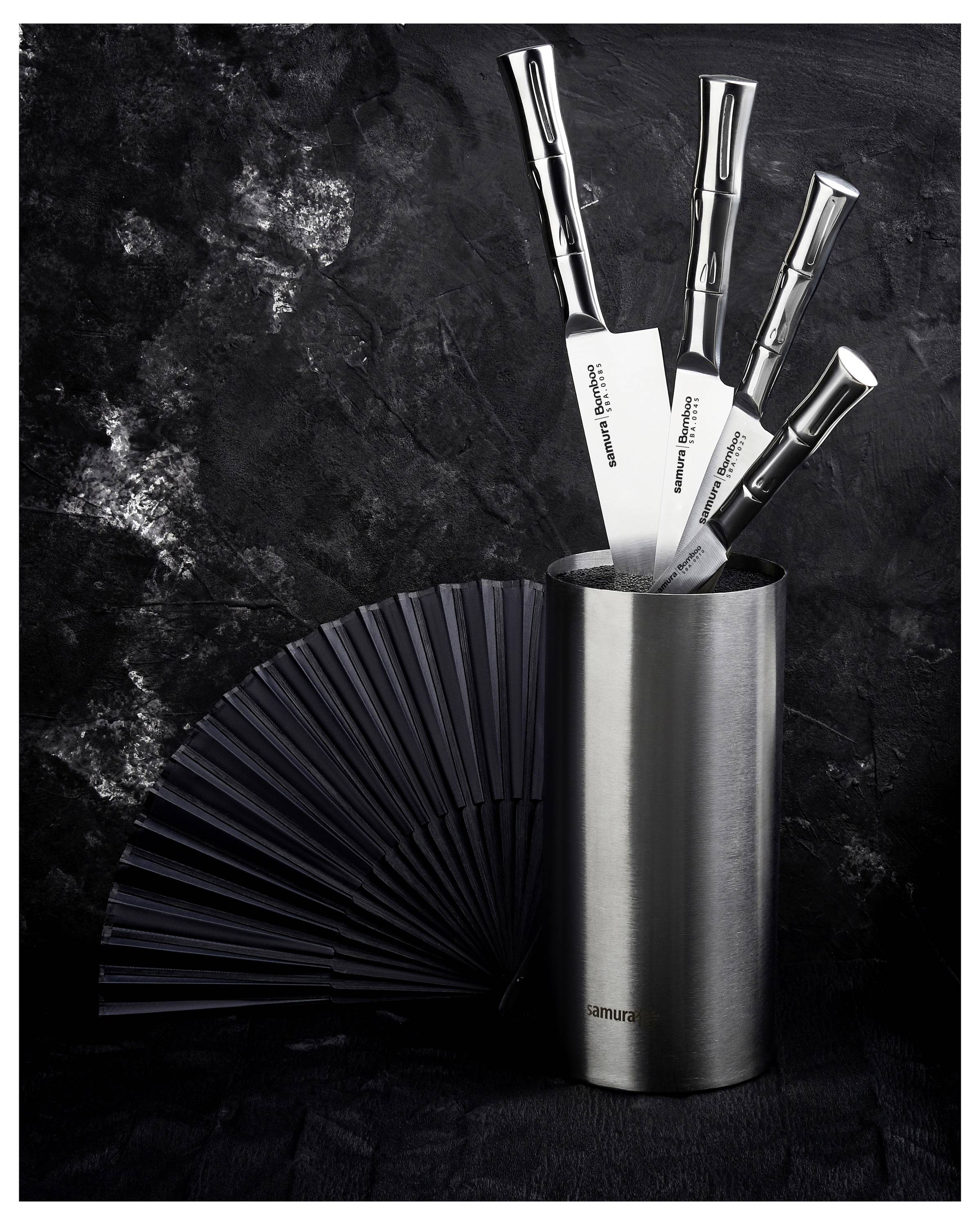 A sleek set of stainless steel knives in a modern holder with a black fan in the background, set against a textured dark surface.