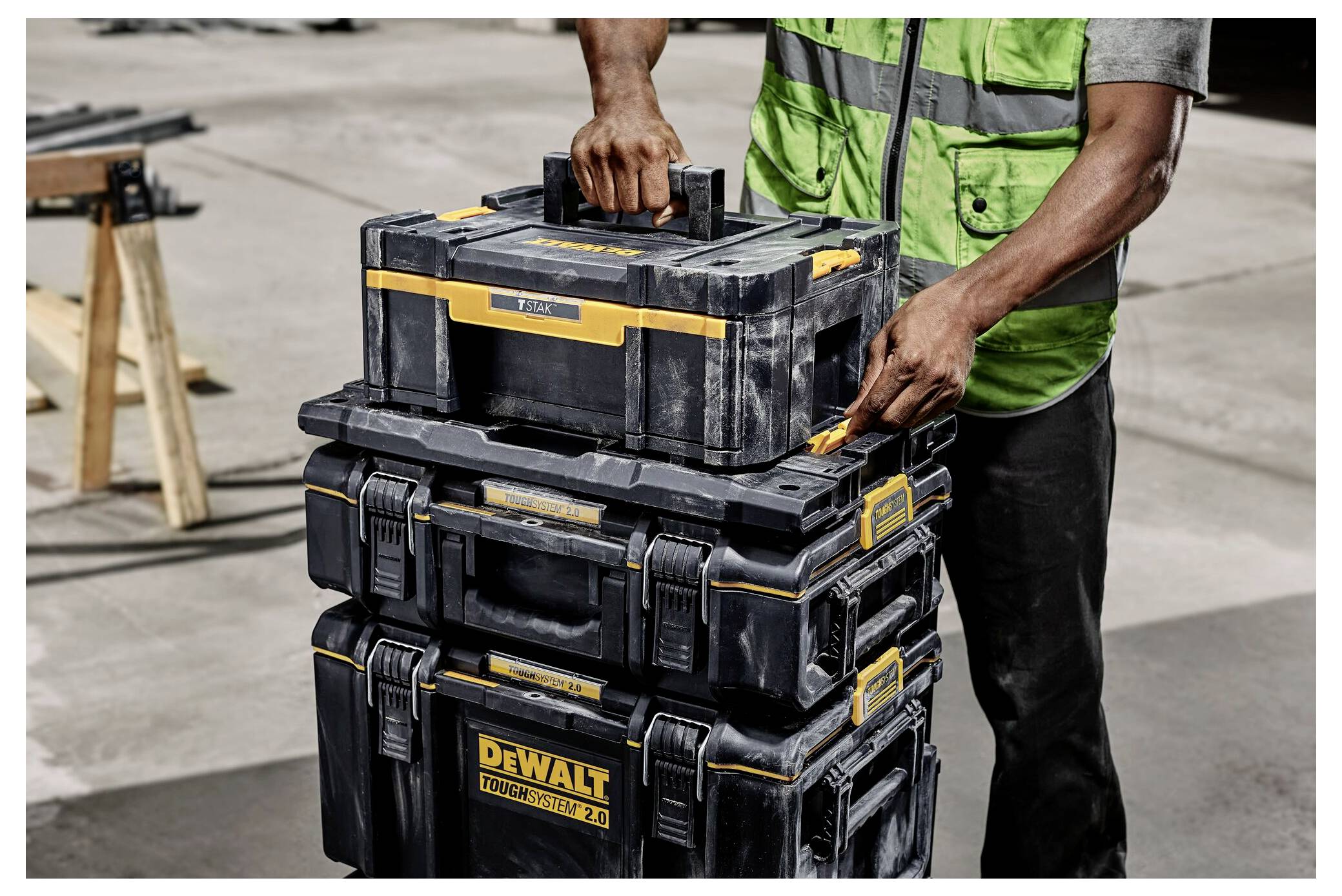 Un travailleur vêtu d'une tenue orange manipule des boîtes à outils DeWalt au bord de l'eau, plusieurs étant empilées sur une surface en béton mouillée.
