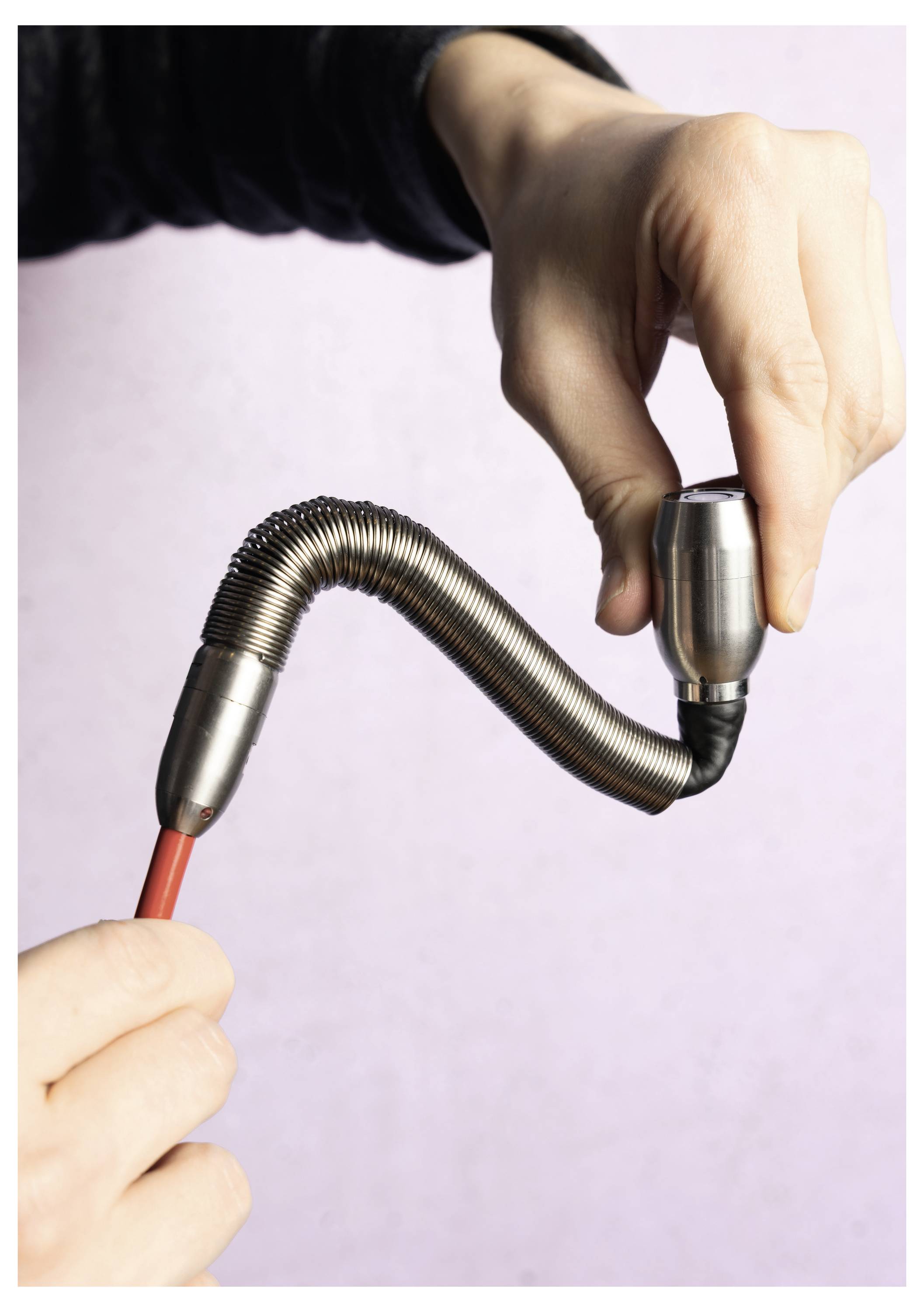 A person's hand demonstrating a flexible metal conduit's bendability by holding and bending it, highlighting its flexibility and control.