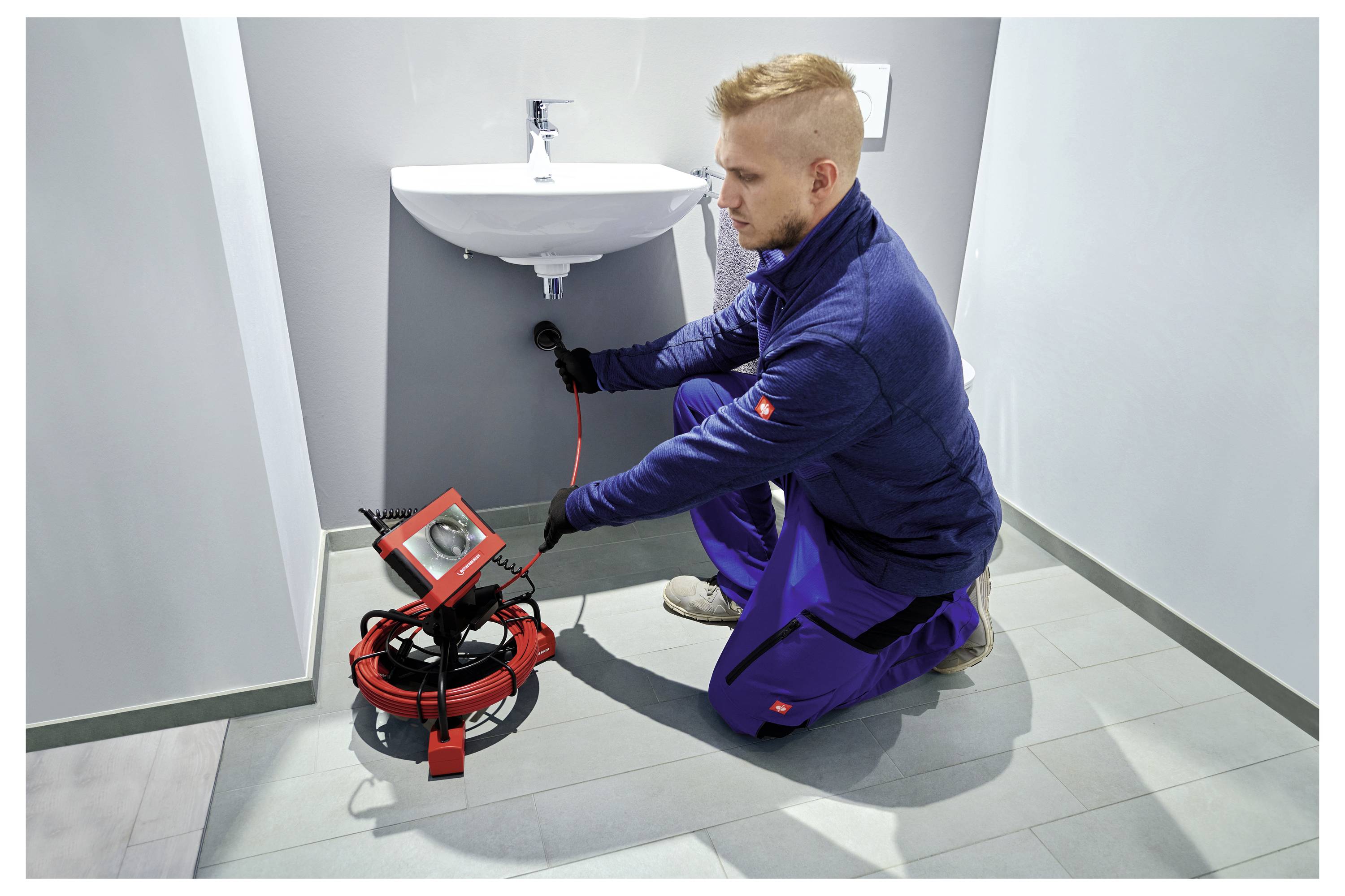 A person is inspecting plumbing under a sink using a camera snake tool in a bathroom.