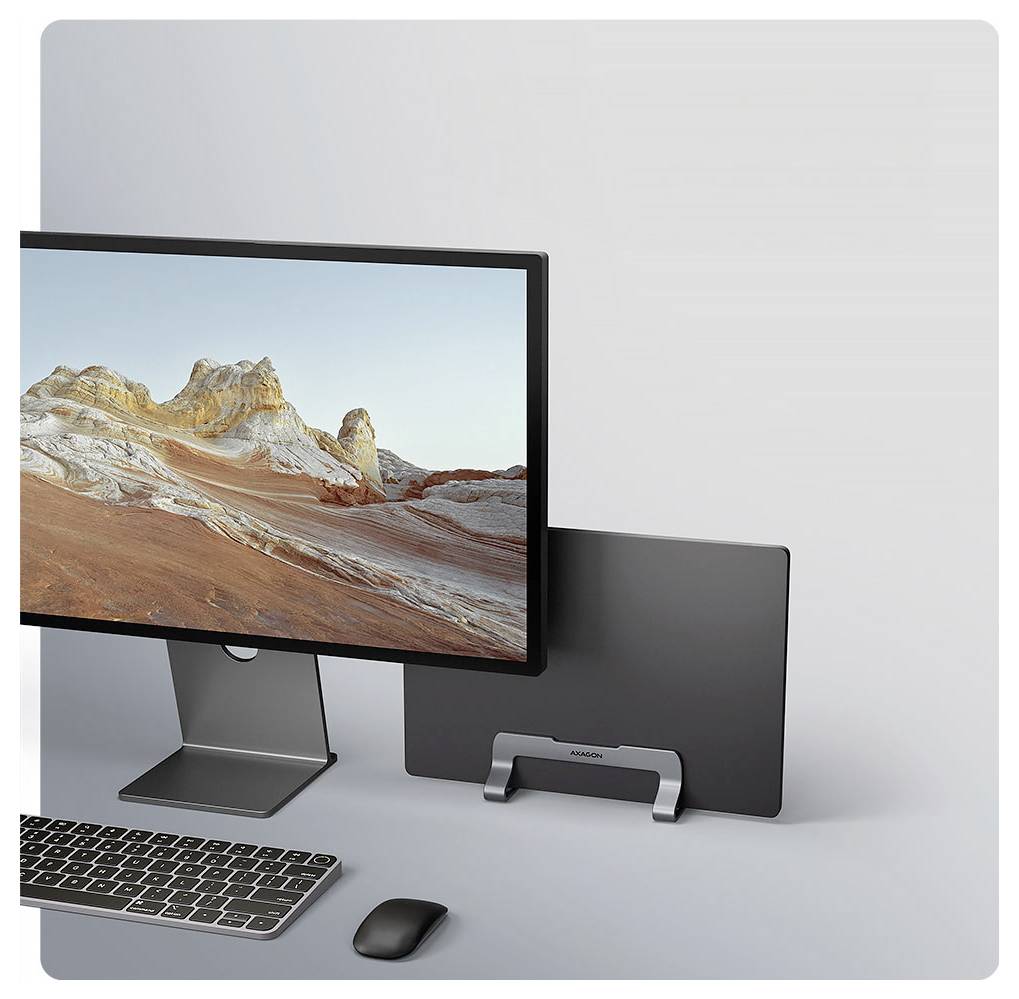 Un moniteur d'ordinateur affichant une image de paysage avec des collines et un ciel lumineux sur un bureau. Un support de laptop élégant maintient un ordinateur portable fermé en position verticale.