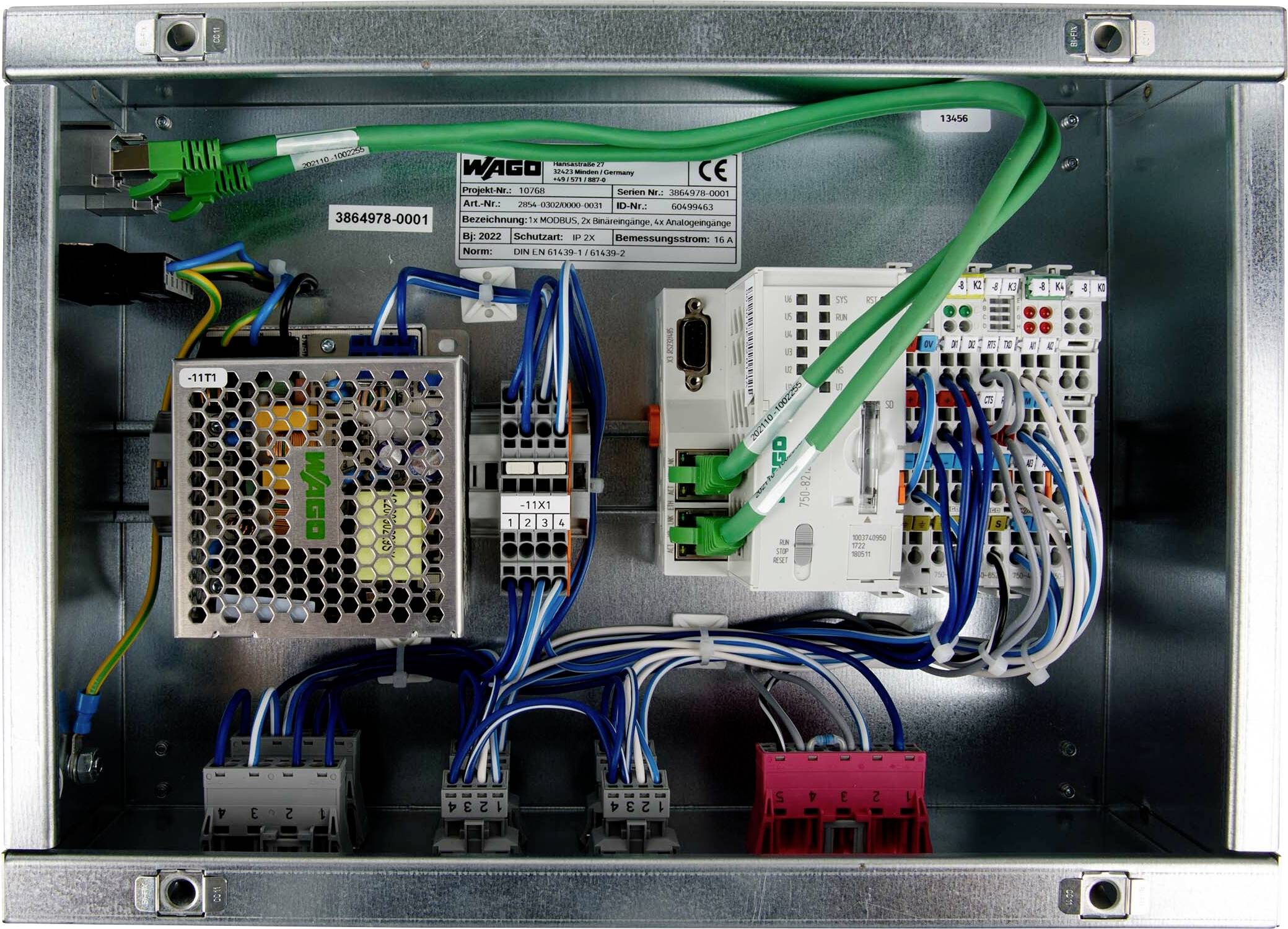 Un panneau de commande électrique ouvert montrant différents fils, cartes de circuits, et une unité d'alimentation électrique disposés à l'intérieur d'un boîtier métallique.