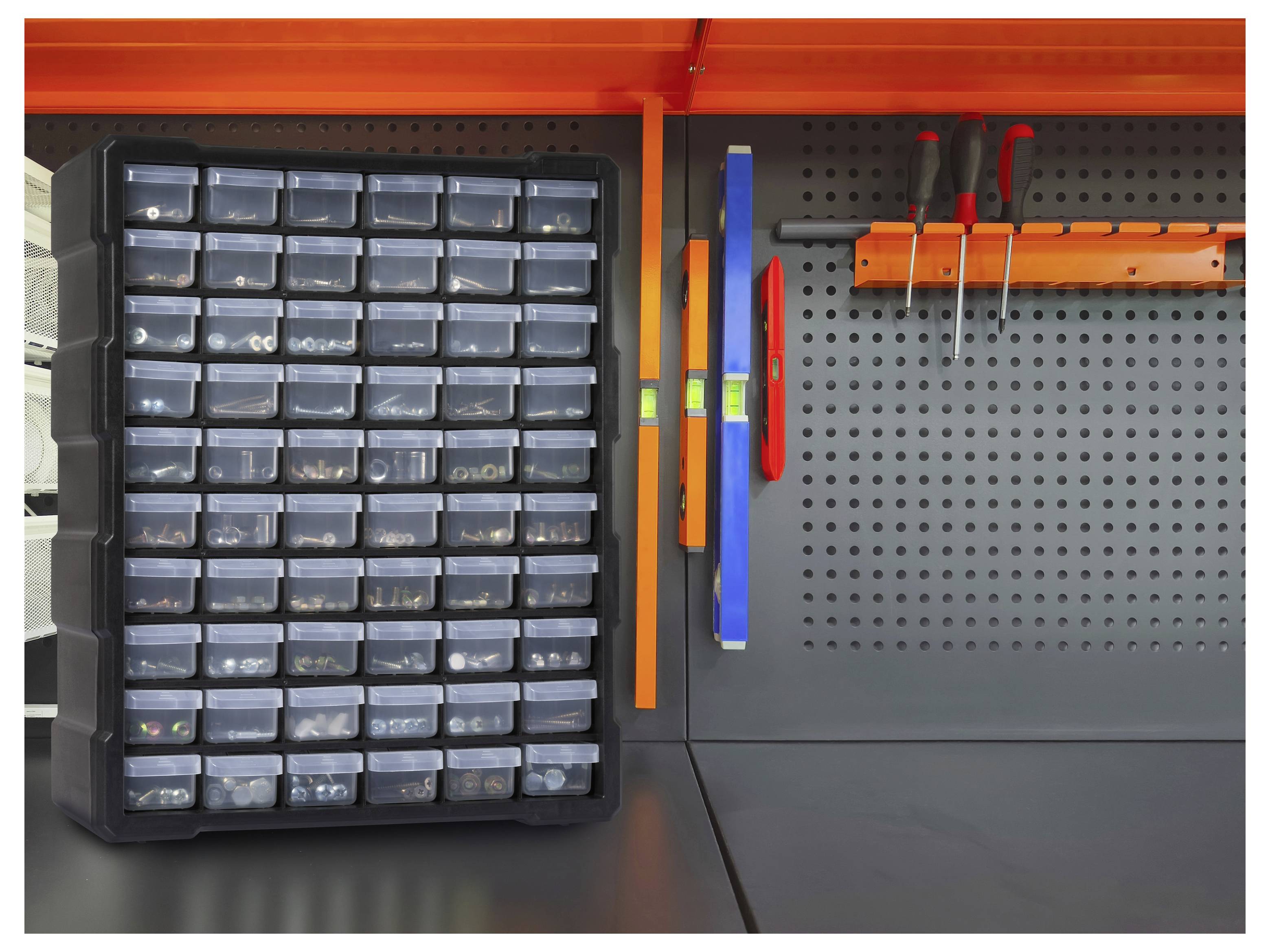 Un organisateur noir monté au mur avec plusieurs tiroirs transparents à côté d'un panneau à chevilles tenant des outils rouges et bleus sur une étagère orange.