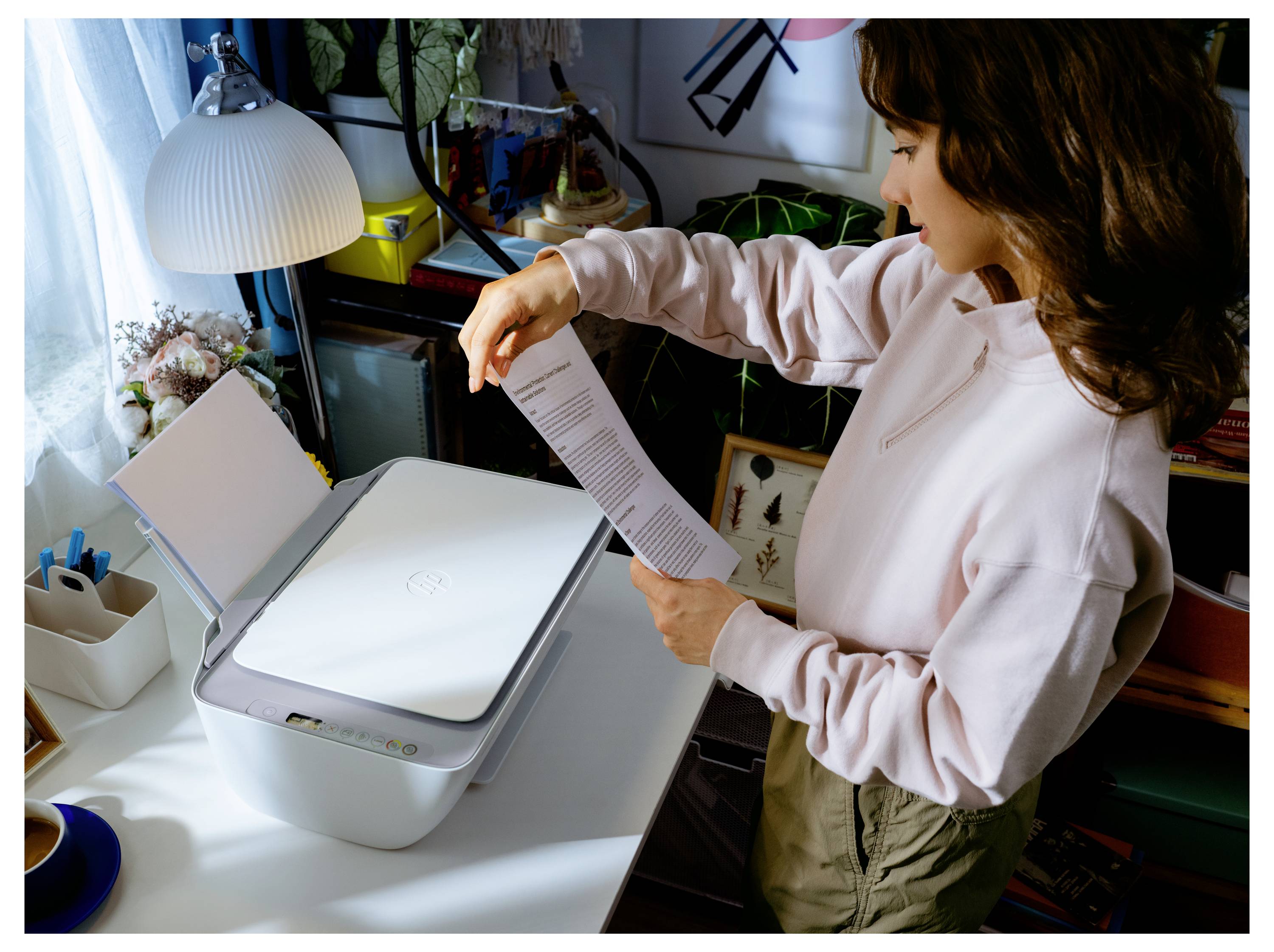 Une personne scanne un document à l'aide d'une imprimante blanche dans un bureau à domicile, entourée de plantes, de livres et de fournitures de bureau.