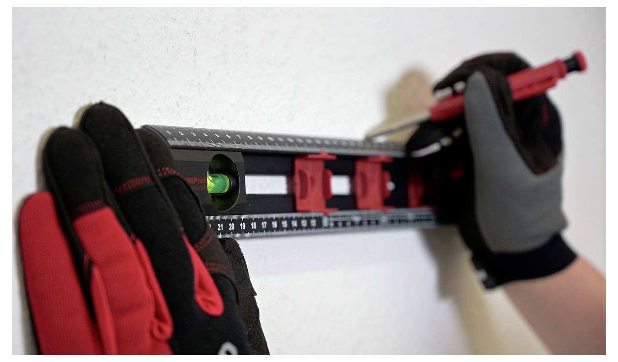 A person wearing gloves uses a level to mark a line on a wall, ensuring it is straight and even.