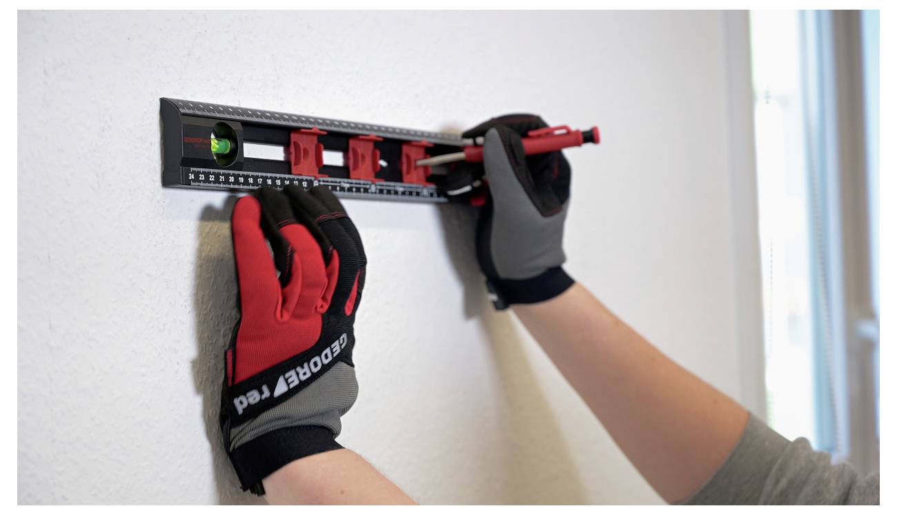 A person wearing gloves uses a spirit level and carpenter's pencil to mark a wall, ensuring alignment and measurement accuracy.