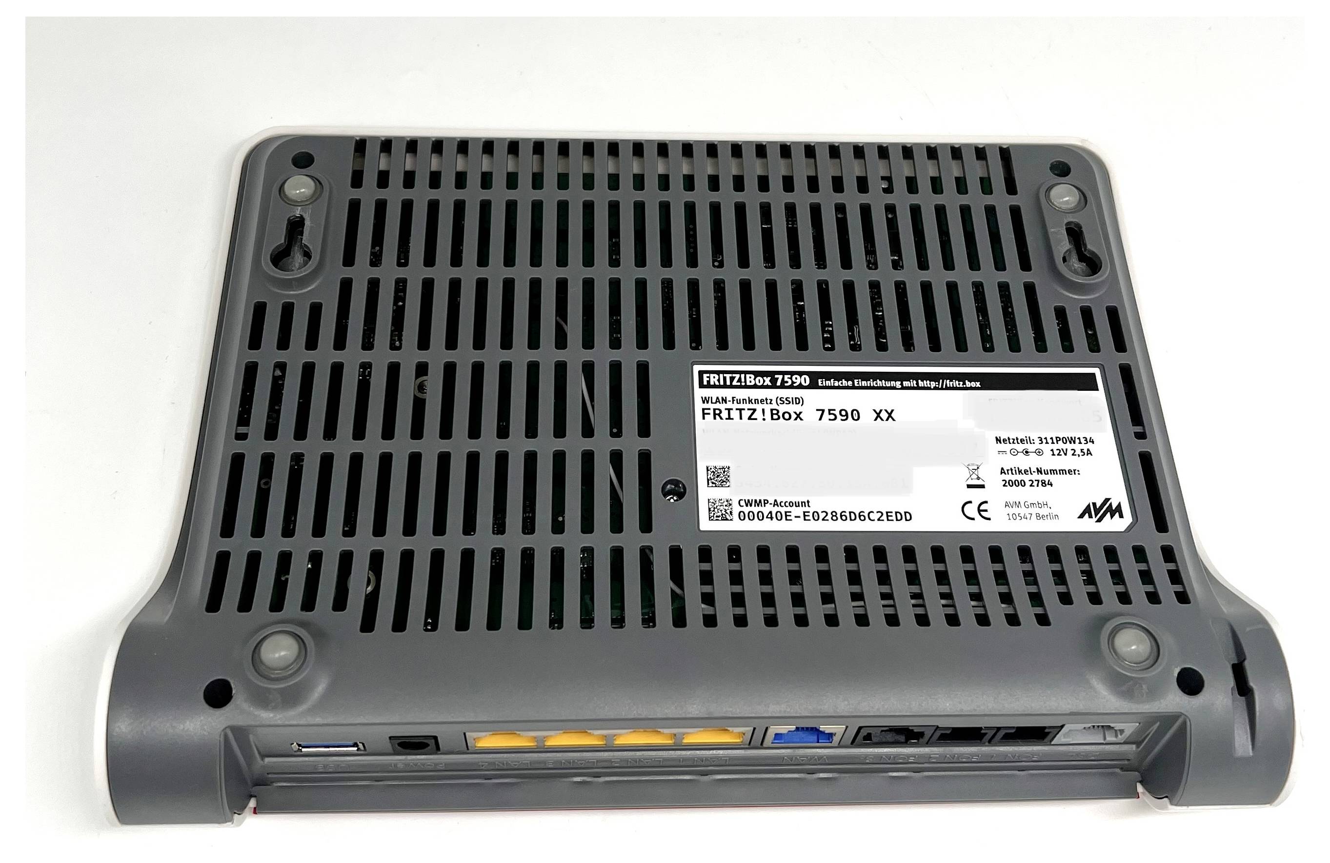 Le dessous d'un routeur FRITZ!Box 7590 montrant les fentes de ventilation, l'étiquette avec le modèle et le numéro de série, ainsi que les ports de connexion réseau.