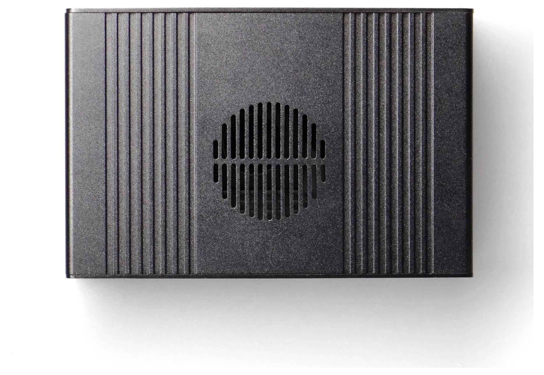 Une boîte de haut-parleur rectangulaire noire avec des rainures verticales et une grille circulaire centrale est présentée vue de dessus sur un fond blanc.