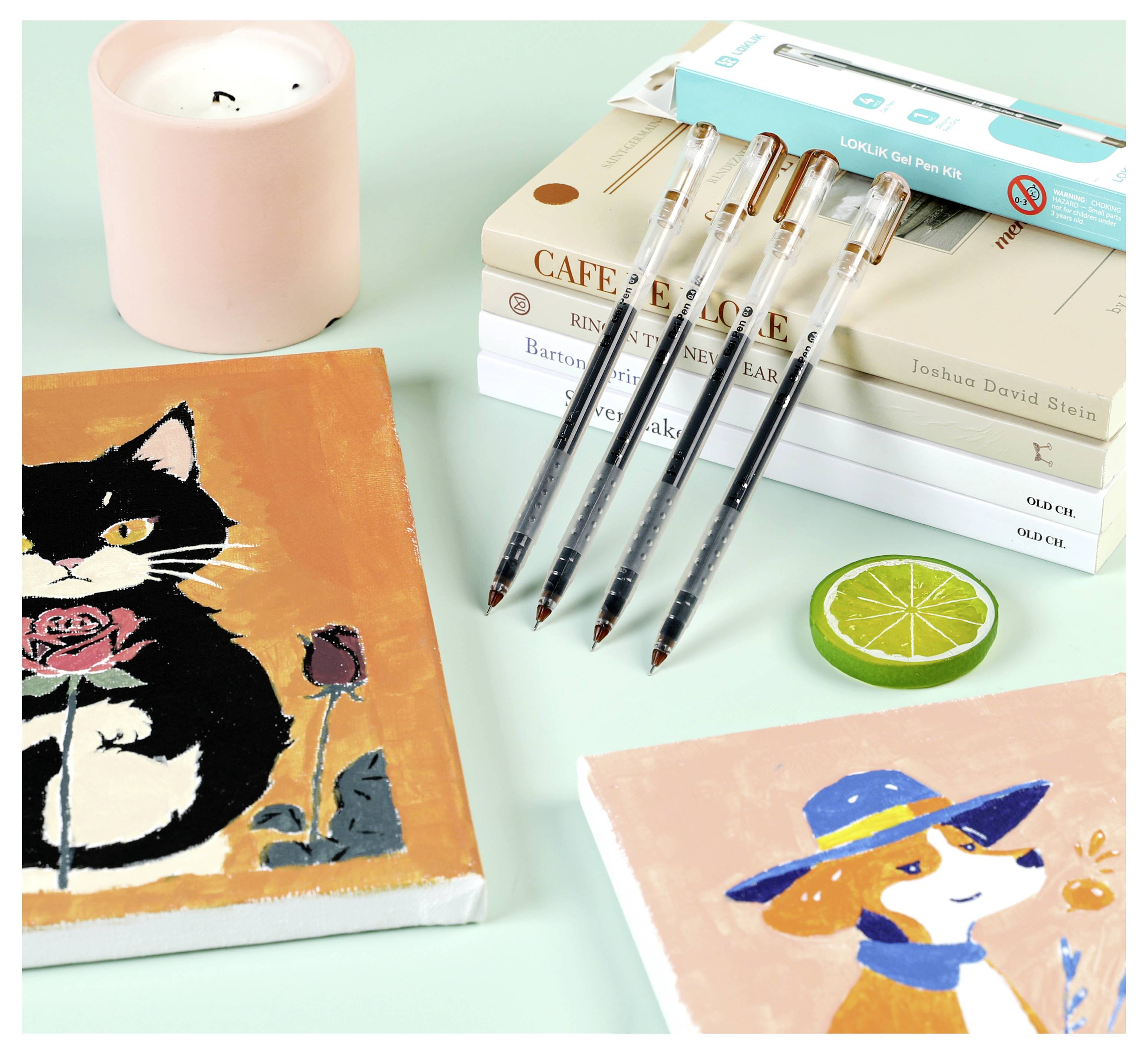 « Fournitures artistiques et livres sur un bureau ; comprend des peintures d'un chat avec une rose, d'un chien avec un chapeau, des stylos, une bougie et des livres empilés. »