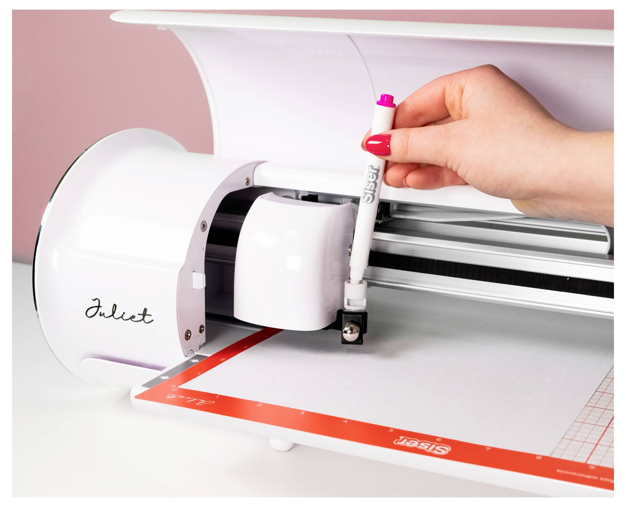 Une personne insère un stylo dans une machine de découpe intitulée « Juliet », la préparant à dessiner ou à découper sur une feuille avec des contours.