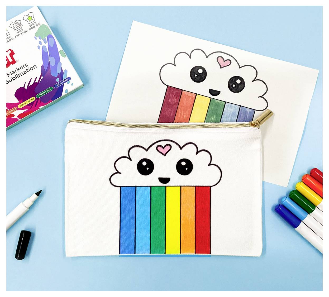 Une pochette avec un motif de nuage et d'arc-en-ciel repose sur une surface bleue à côté de stylos colorés et de son design sur papier.