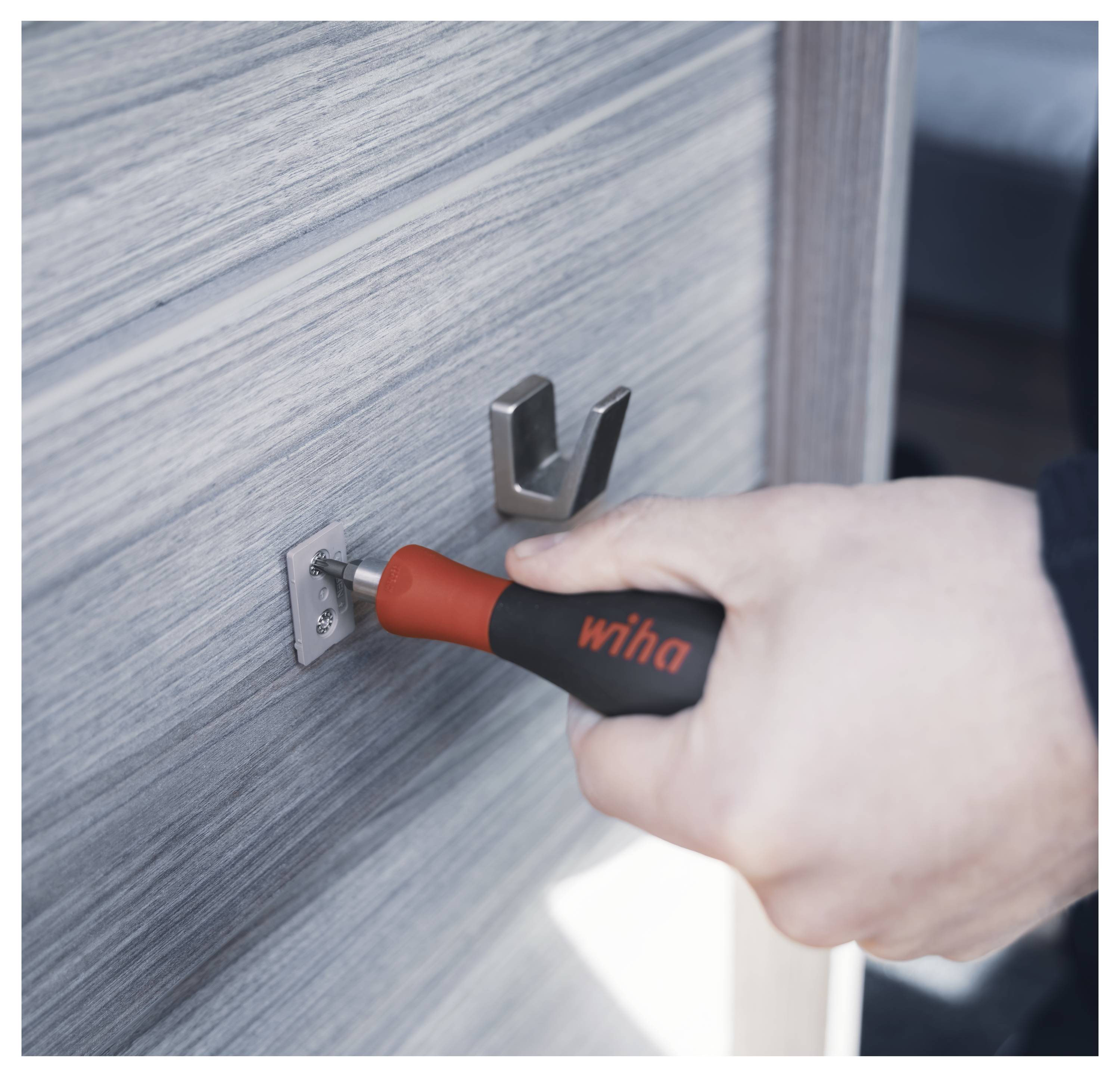 Une main utilise un tournevis Wiha pour serrer une vis sur un support métallique fixé à une surface en bois.