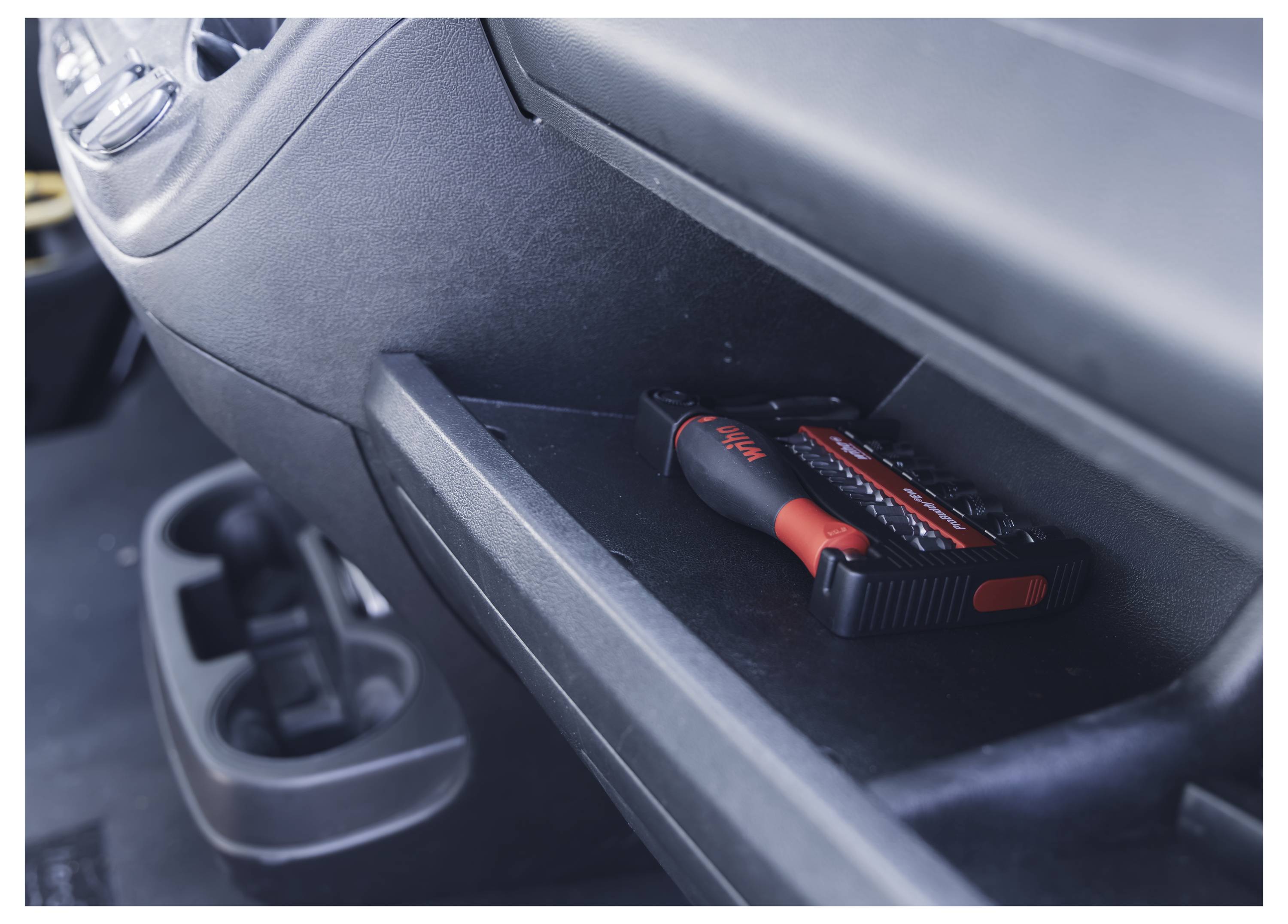 Une trousse d'outils noire et rouge est stockée de manière sécurisée dans la boîte à gants d'une voiture, illustrant le rangement sûr pendant le voyage.