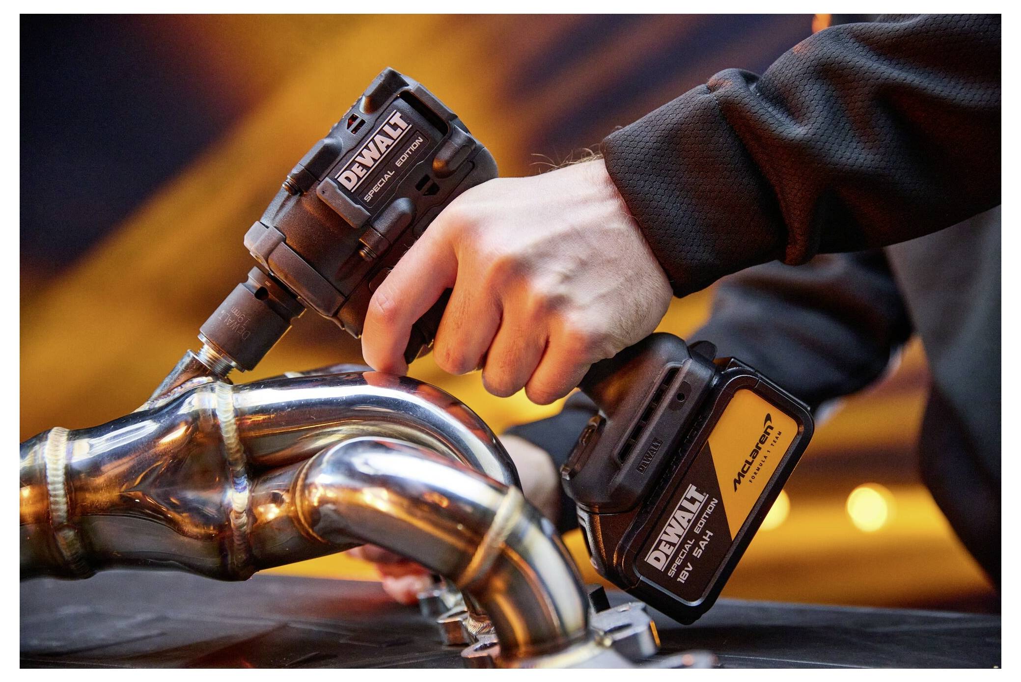 Gros plan des mains utilisant une perceuse sans fil pour serrer des tuyaux d'échappement en métal, avec deux batteries DeWalt visibles.
