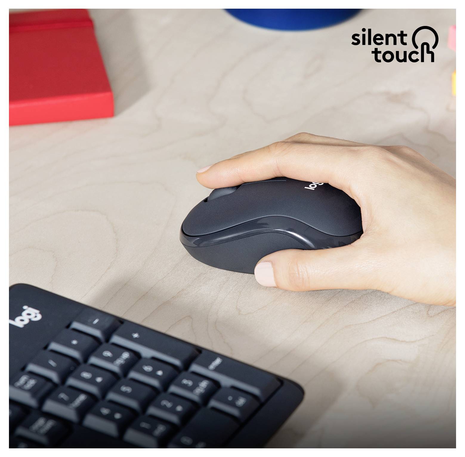 Une main utilisant une souris sans fil noire à côté d'un clavier sur un bureau, avec la marque « silent touch » dans le coin.
